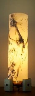 Illuminated cylindrical lamp with marble-like swirl patterns, placed on a dark surface with small square blocks at base.