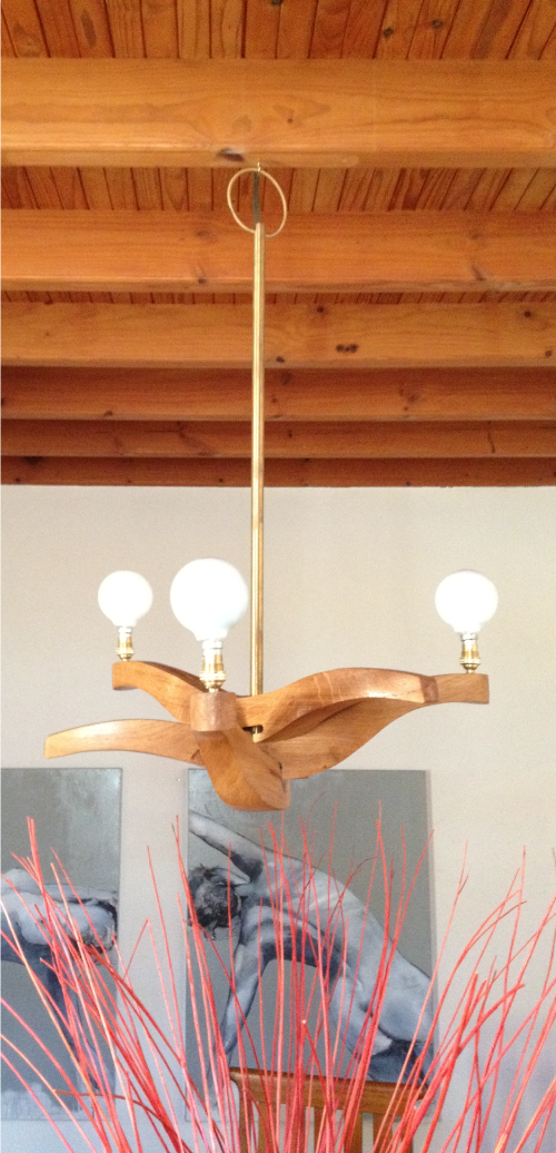 Wooden chandelier with three light bulbs hanging from a ceiling with wooden beams.
