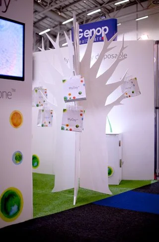 White paper tree display with product packages hanging from its branches at an exhibition booth.