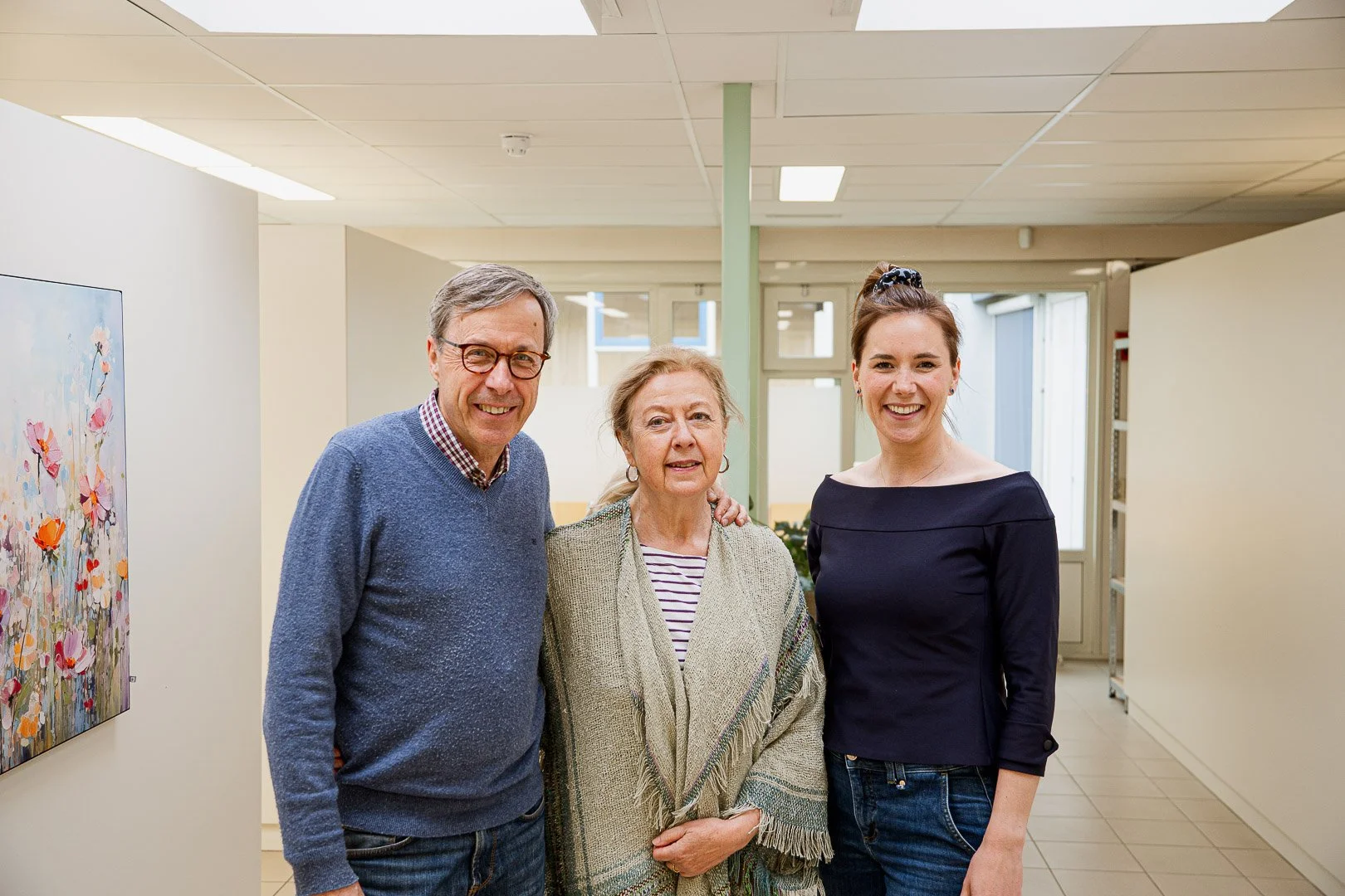 Three people, two women and one man, standing together inside a brightly lit art gallery, smiling at the camera.