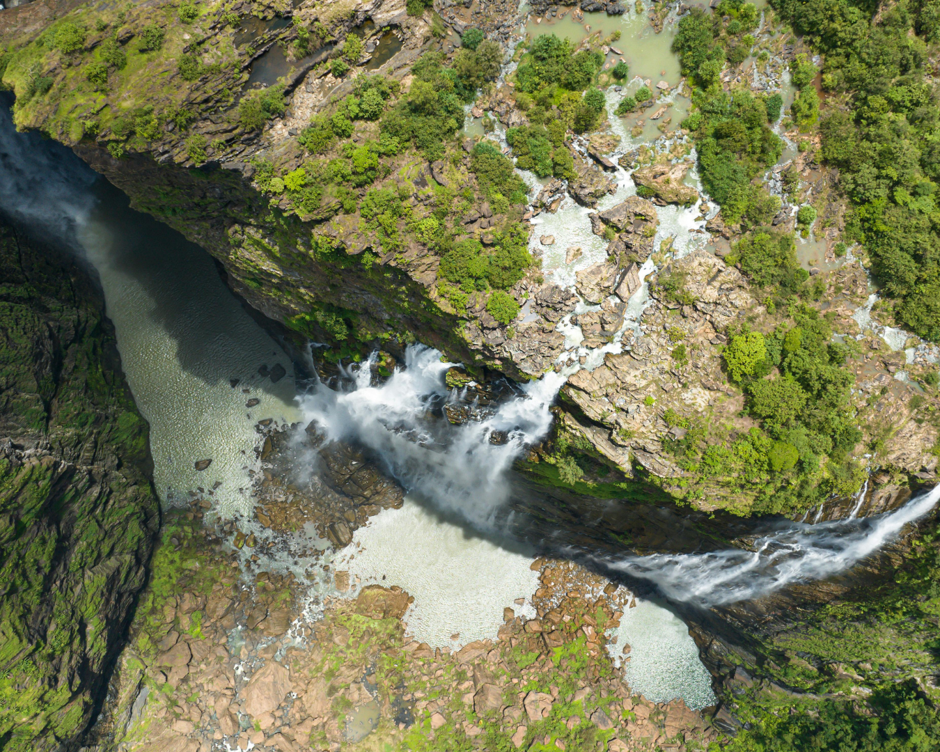 An aerial photo of a waterfall and the gorge below amidst greenery