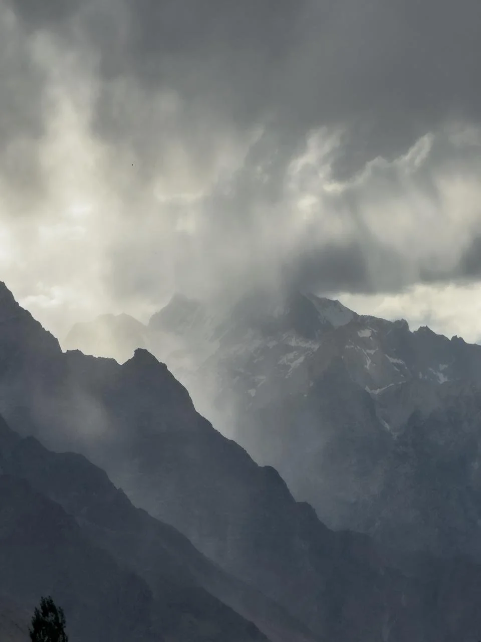 Snow-capped mountain peaks under a cloudy, stormy sky with mist and dense clouds surrounding the mountains.