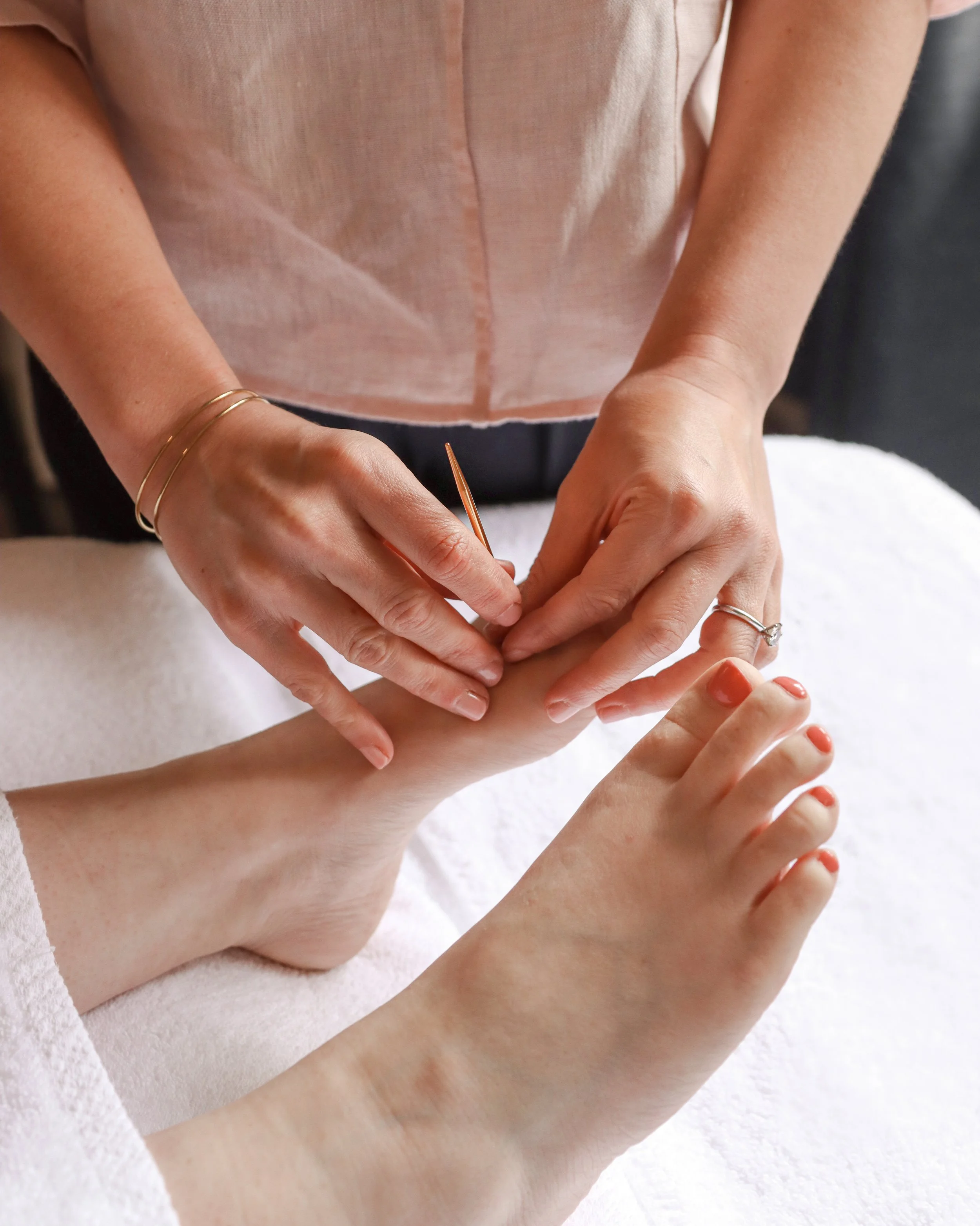 Person getting a manicure, with a focus on their feet and hands, while another person applies nail polish to their toenails.