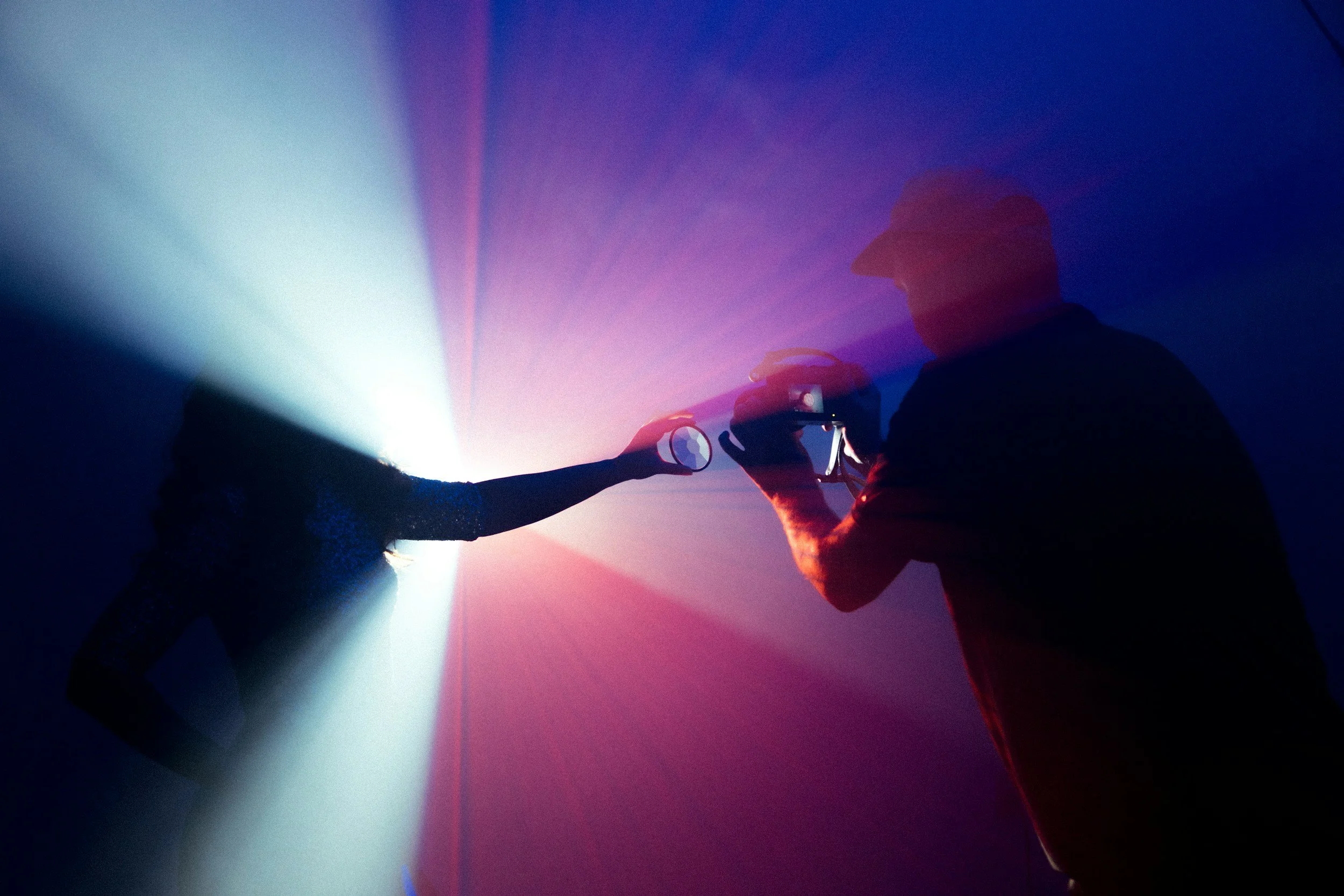 A person taking a photo of a woman in front of bright, colorful light beams.