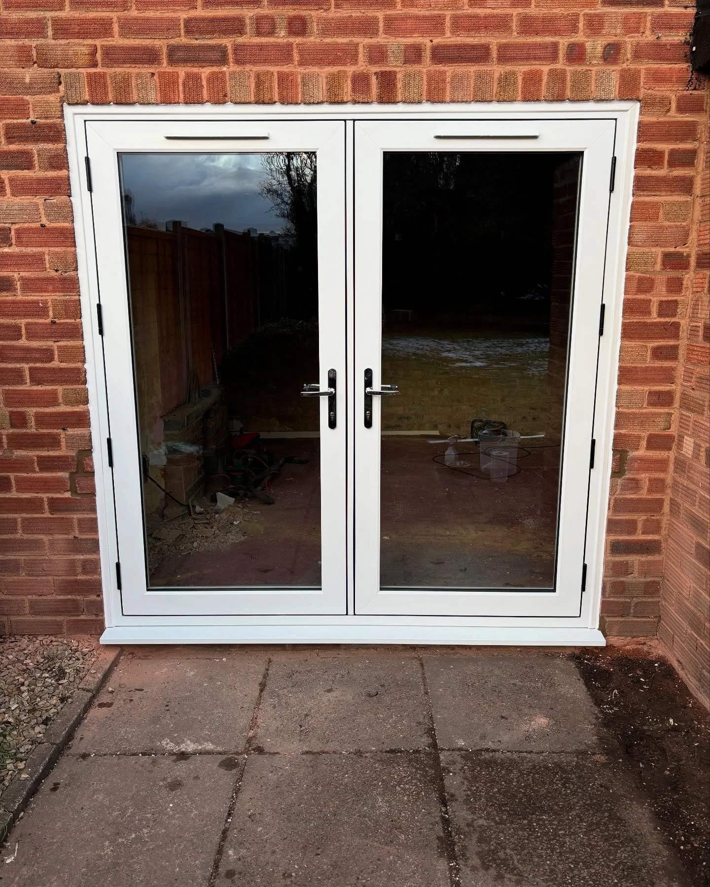 White-framed glass patio doors leading to an outdoor area with brick wall and paved concrete ground.