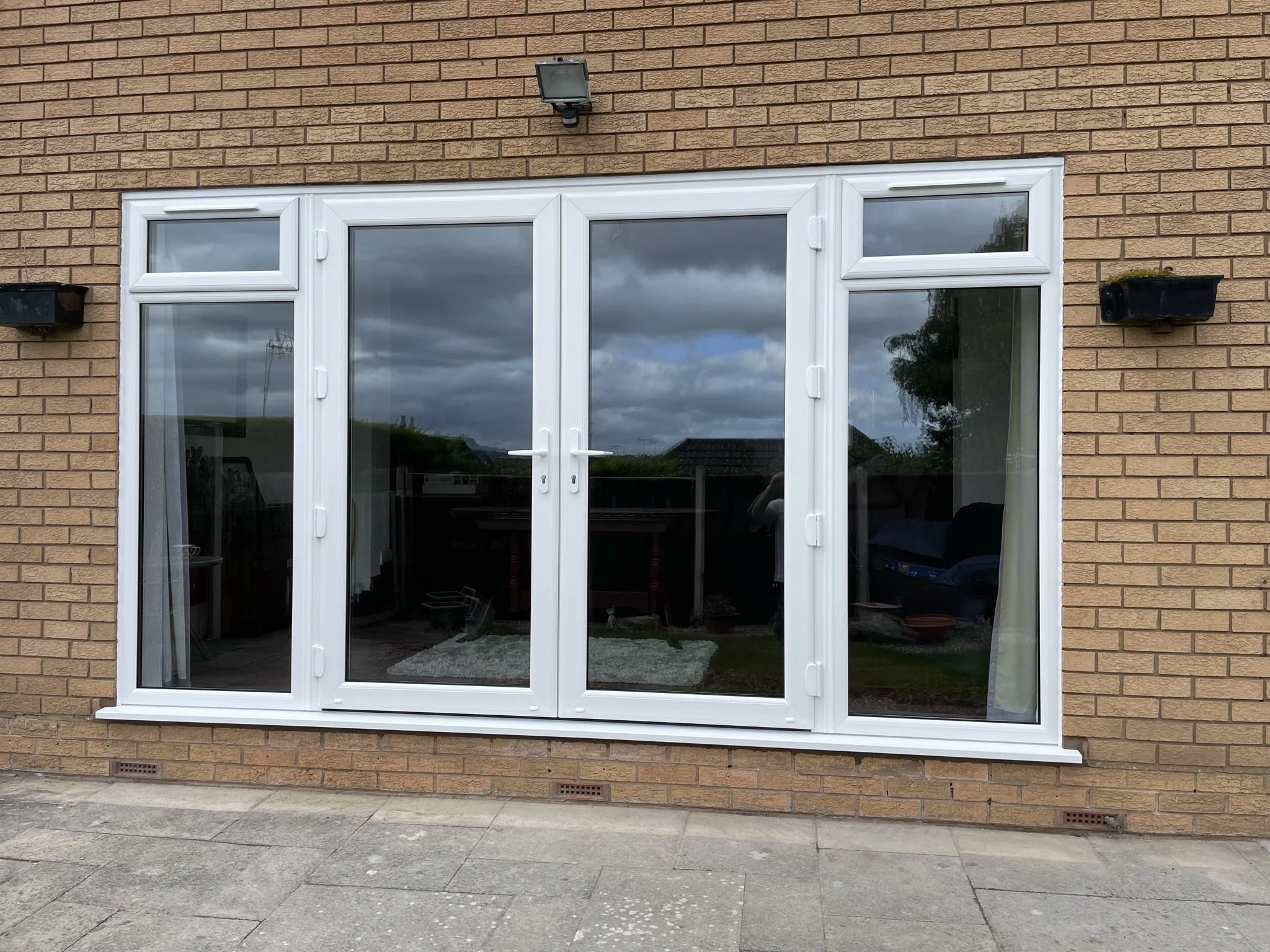Reflective glass door with side panels on a brick house exterior, with a dark outdoor light fixture above.