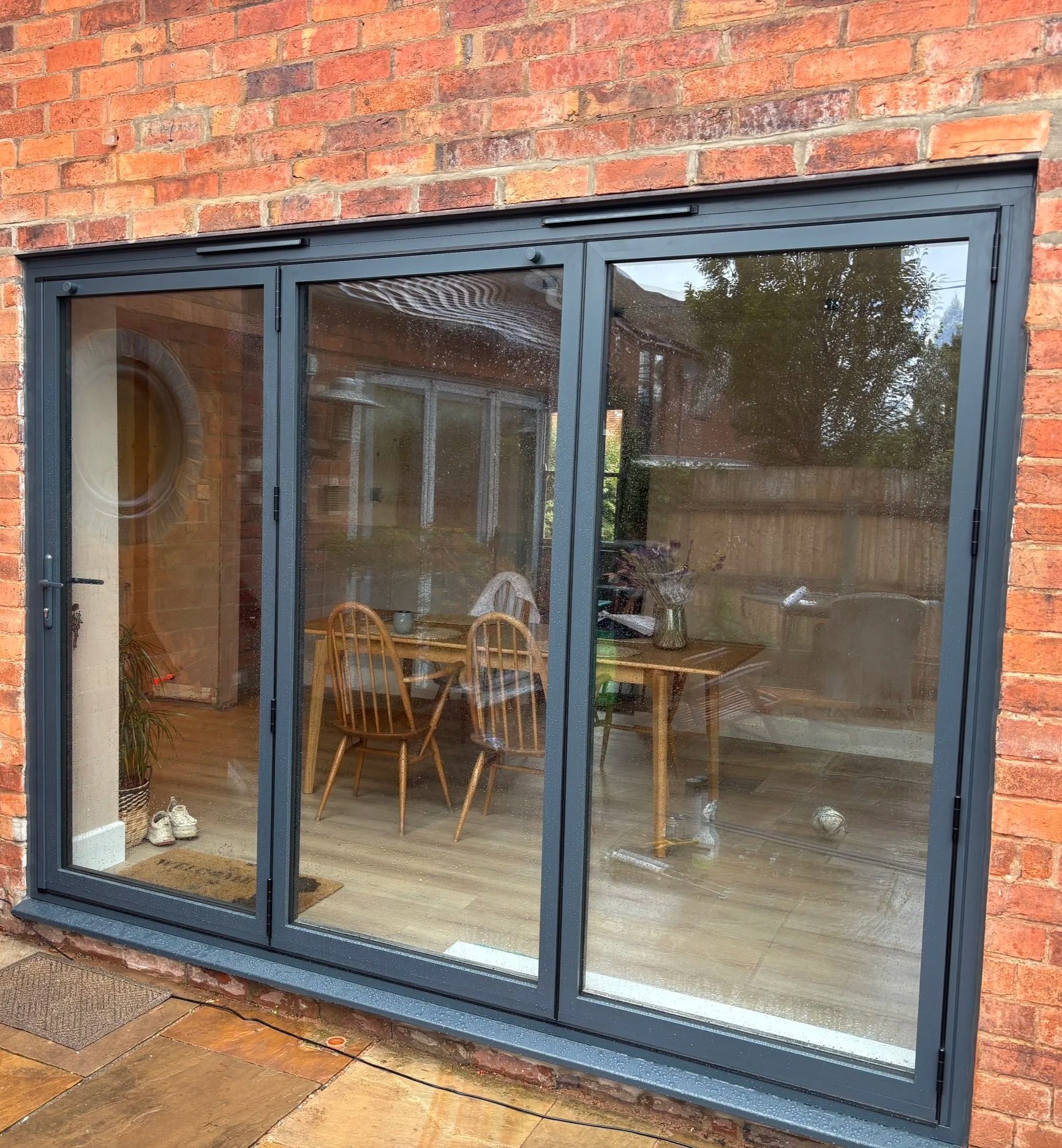 View of a glass sliding door leading into a dining area with wooden chairs and a table, brick exterior wall, and an outdoor patio.