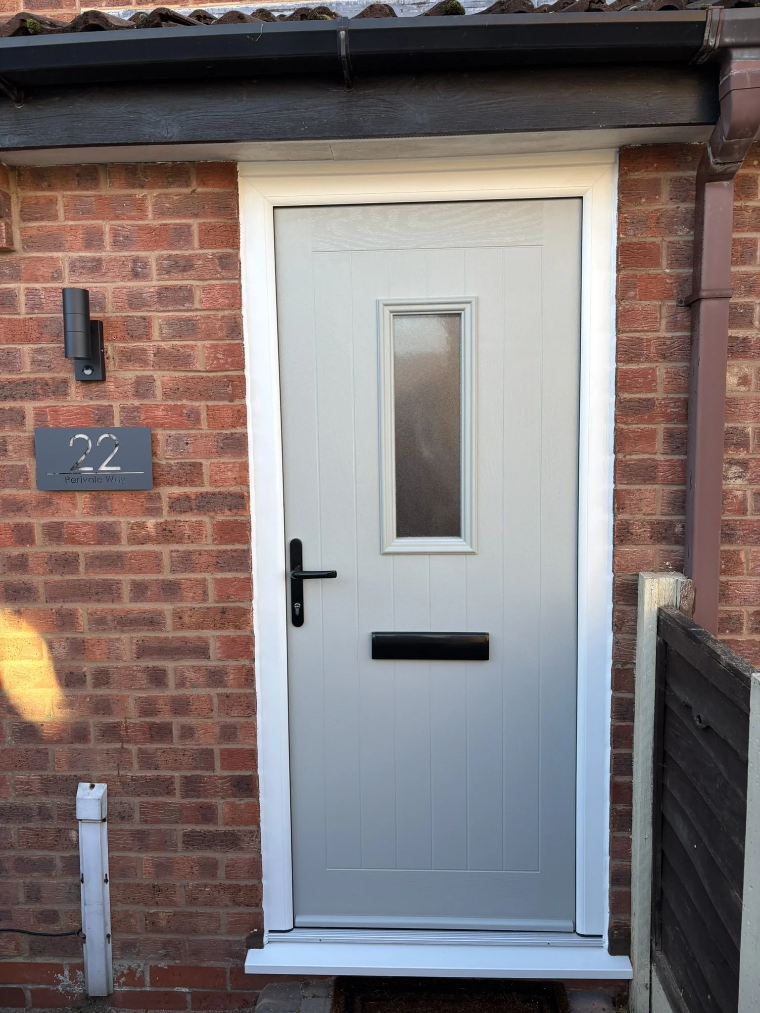 Front entrance door of a house with a brick wall, house number 22, a letterbox, and a small black wall-mounted light fixture.