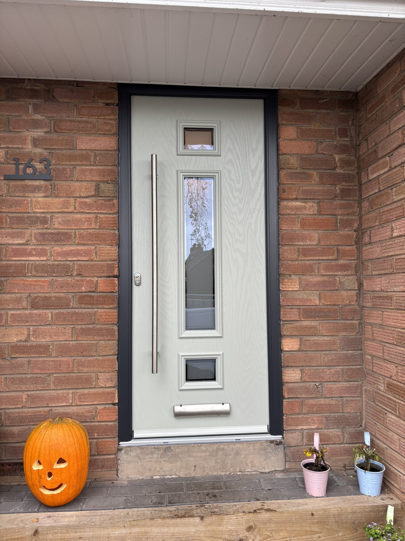 Front door of a house with a pumpkin decoration on the left and two potted plants on the right.