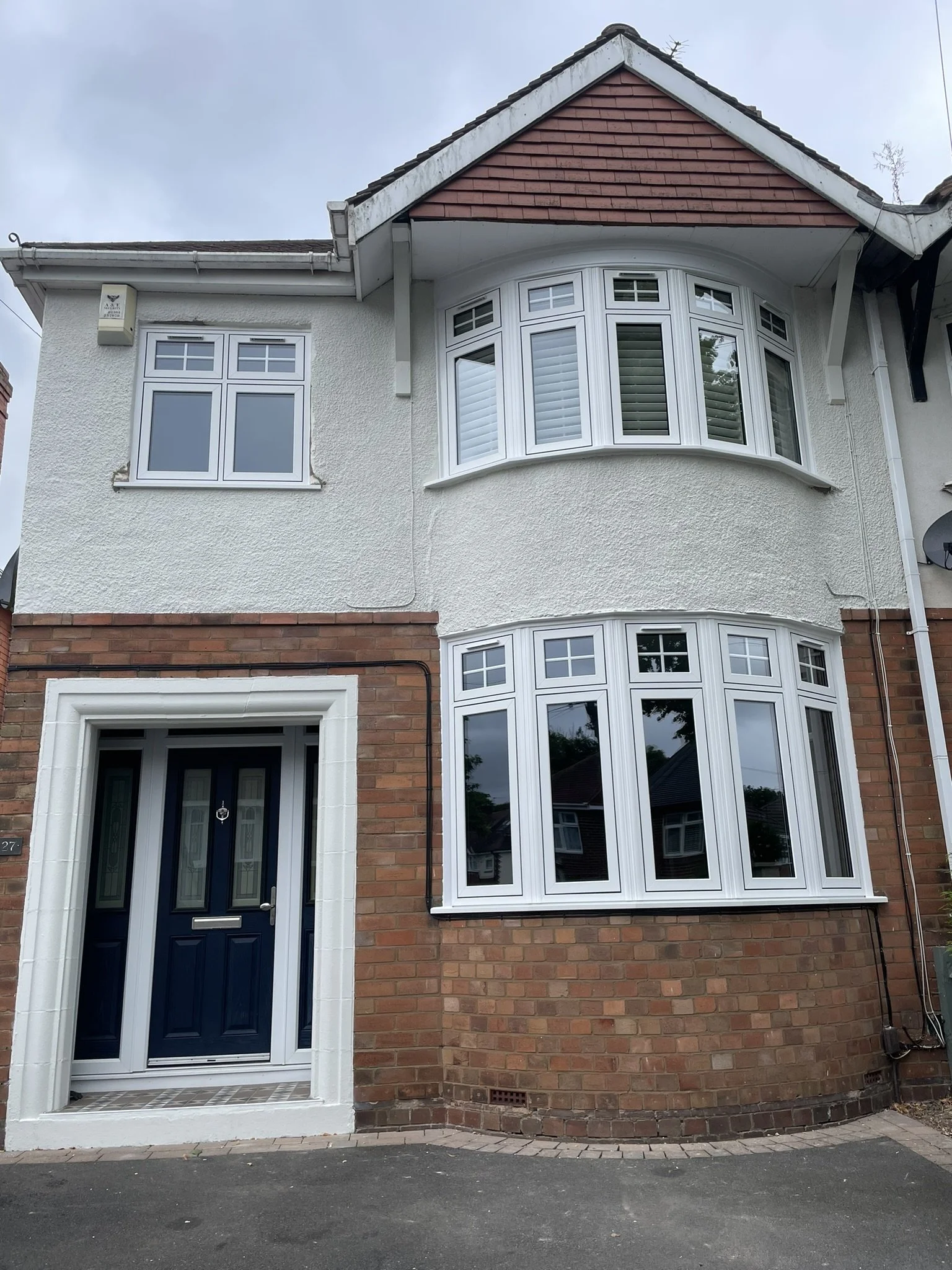 A multi-story house with a brick and white stucco exterior, featuring bay windows and a dark blue front door.
