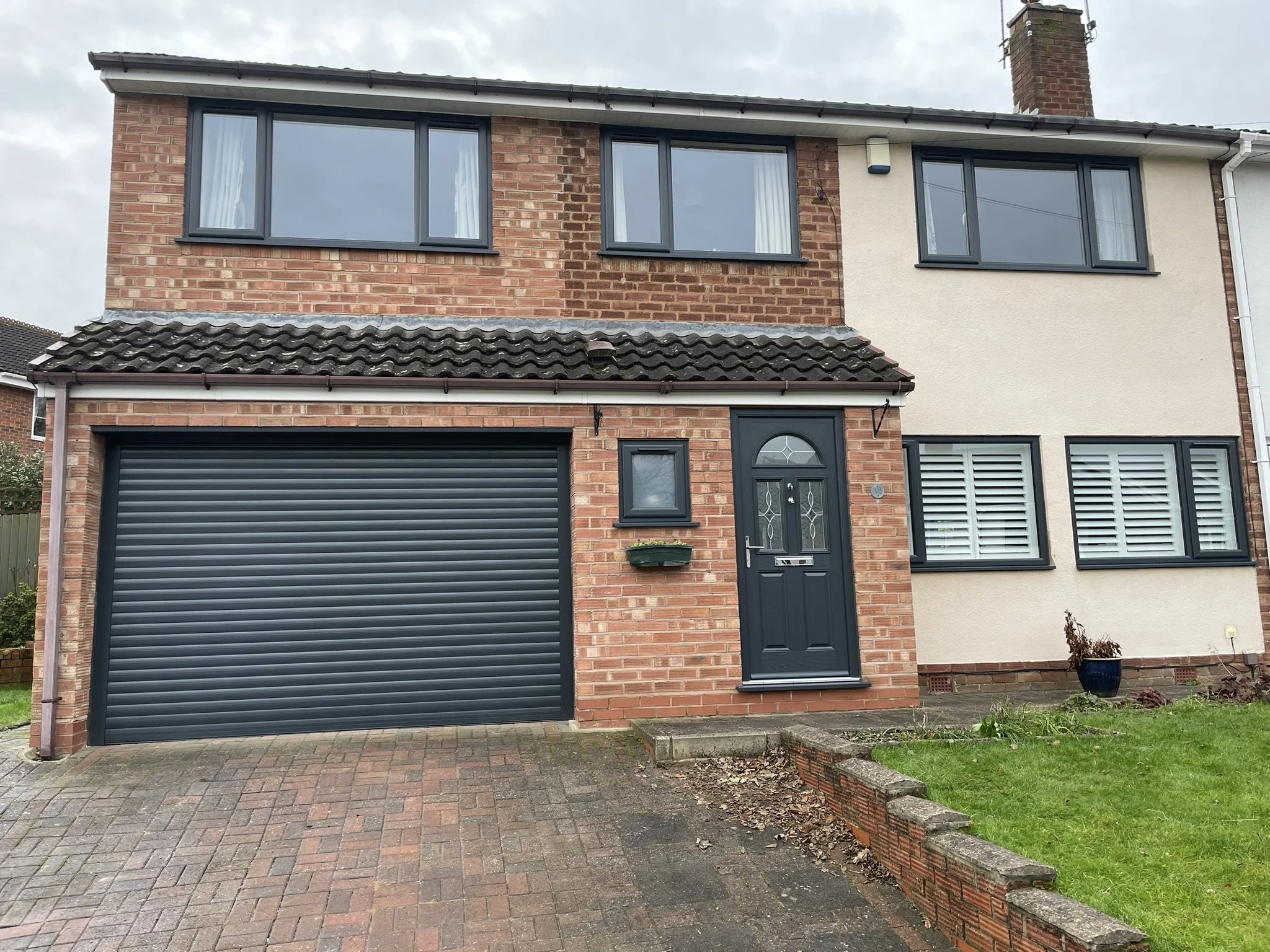 Front view of a two-story house with a brick exterior, black garage door, black front door with a decorative window, and a small green lawn.
