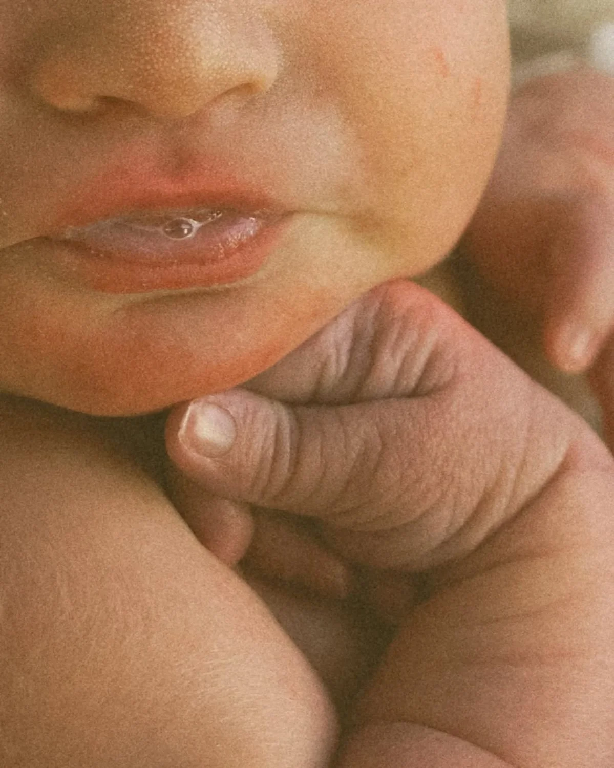 Close-up of a child's face with slightly parted lips, and a hand touching the child's chin.