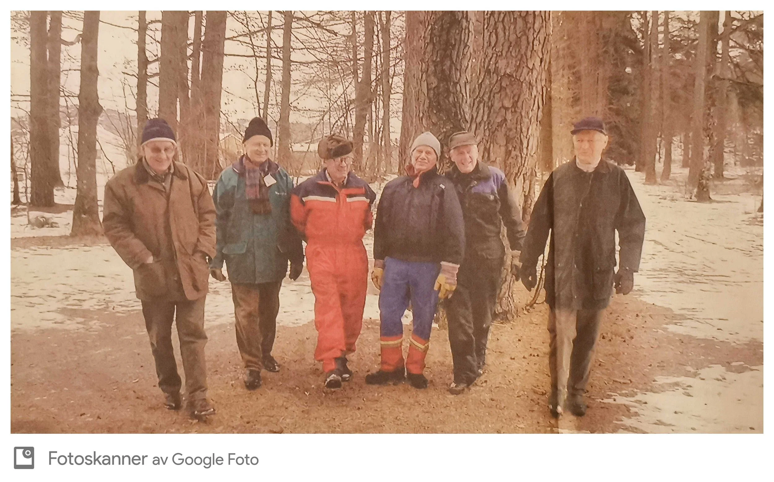 Seks personer som står i en skog om våren eller høsten, alle kledd i varme klær med vinterhatter og jakker.