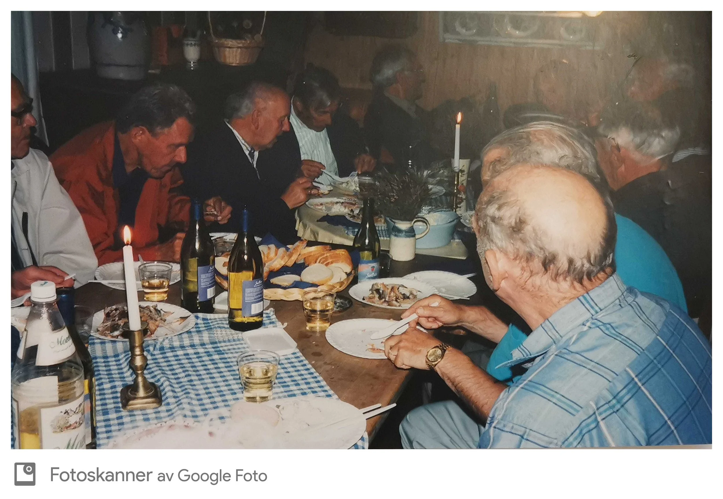 En gruppe eldre menn sitter rundt et bord og spiser, med lys og mat på bordet, i en koselig innendørs setting.