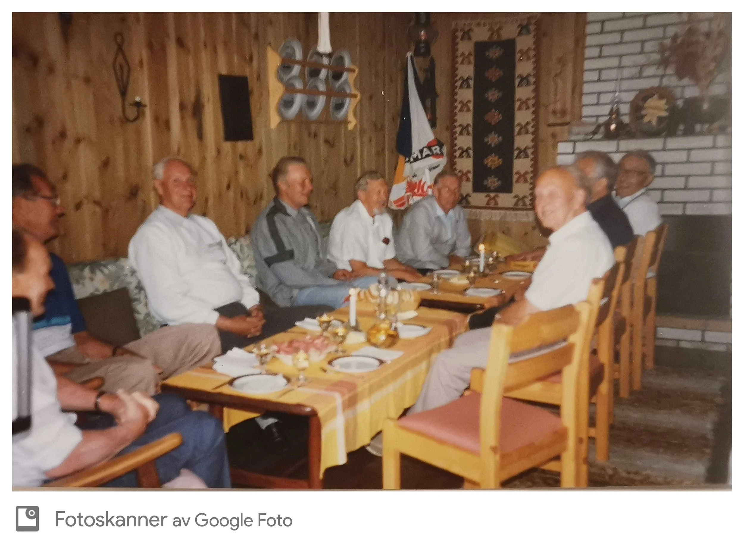 En gruppe eldre mennesker sitter rundt et spisebord i et rom med trepanel på veggene