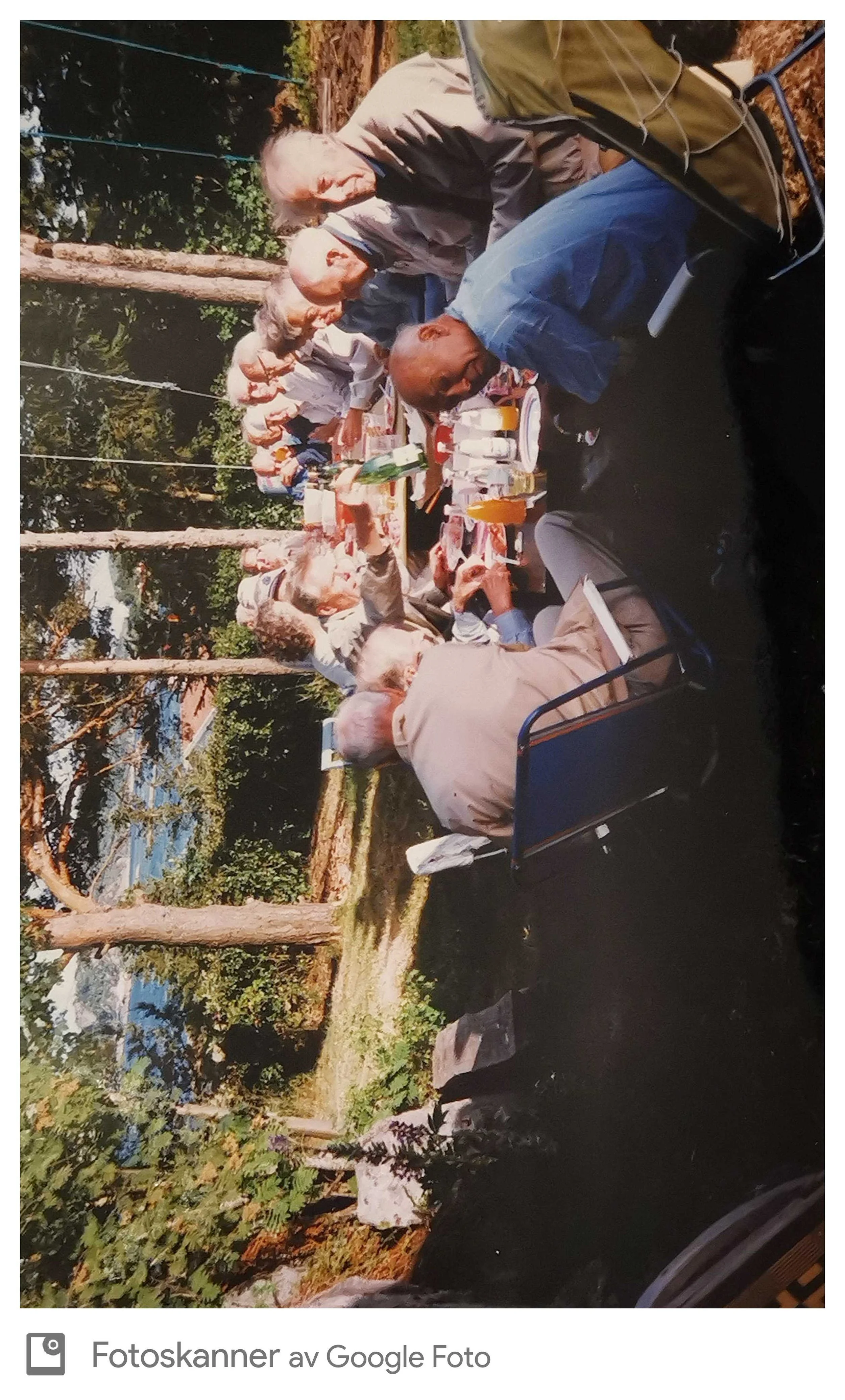 Grupp mennesker som spiser utendørs ved en lang bord i en skogkledd park.