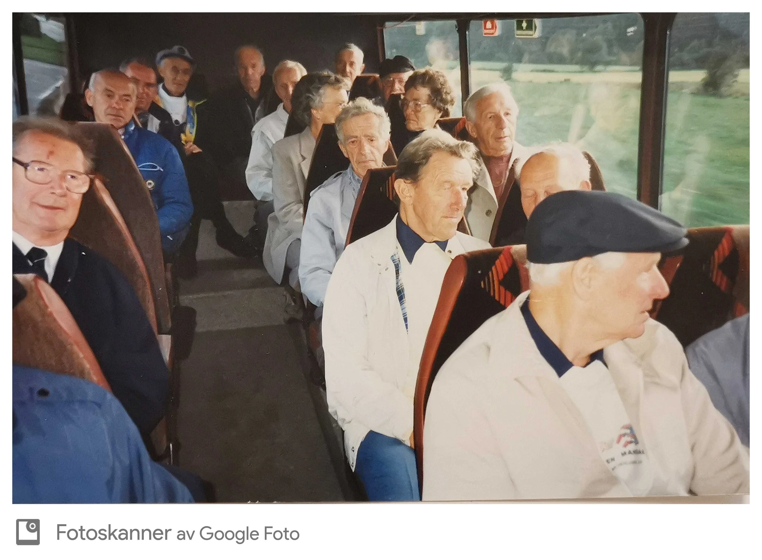 Bilde av en gruppe eldre personer som sitter i en buskø, de ser ut til å være i en bussturreise. Noen personer har på seg jakker og hatt, og de ser ut til å være rolige og forsøker å følge med på noe utenfor bussen.