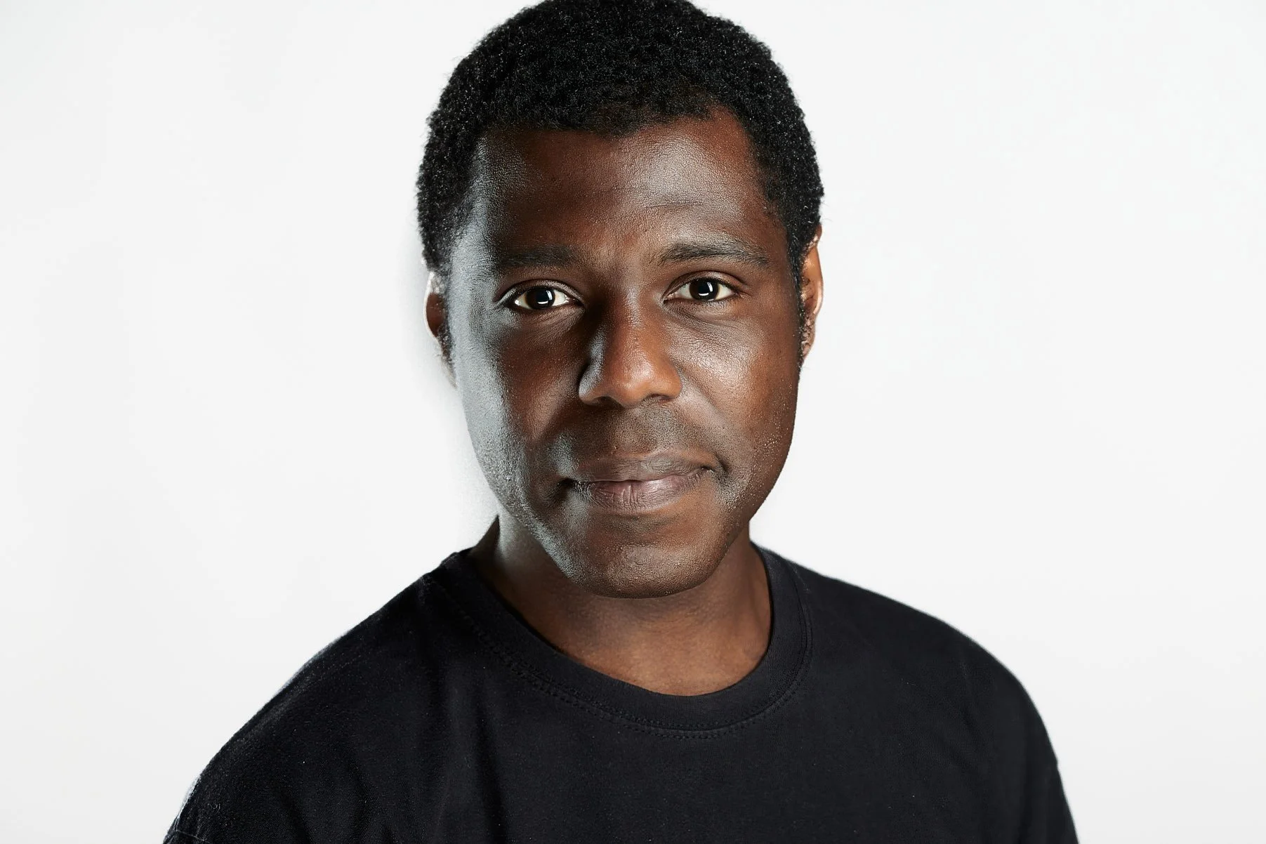 Headshot of a professional businessman with dark skin and short curly hair wearing a black shirt against a white background.