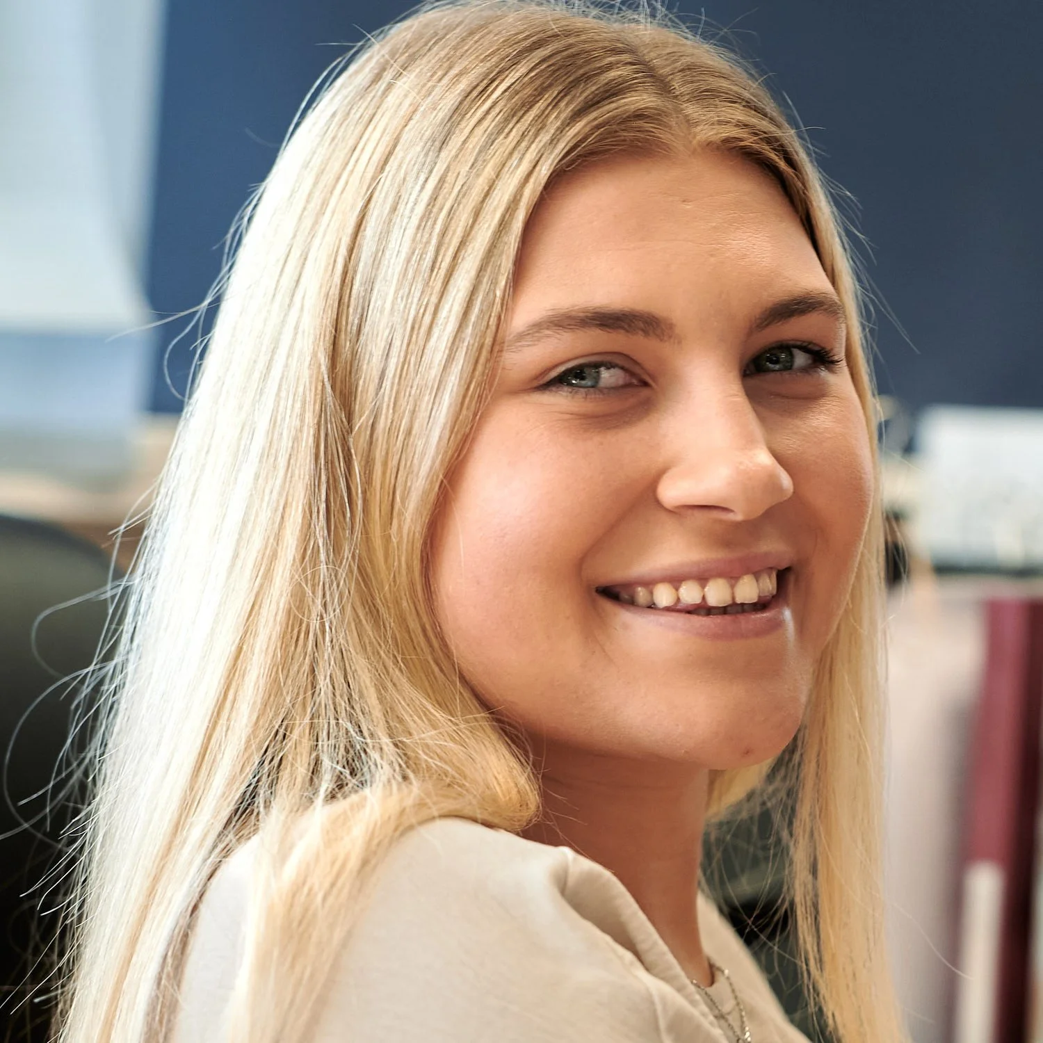 A woman with long blonde hair smiling in an indoor setting.
