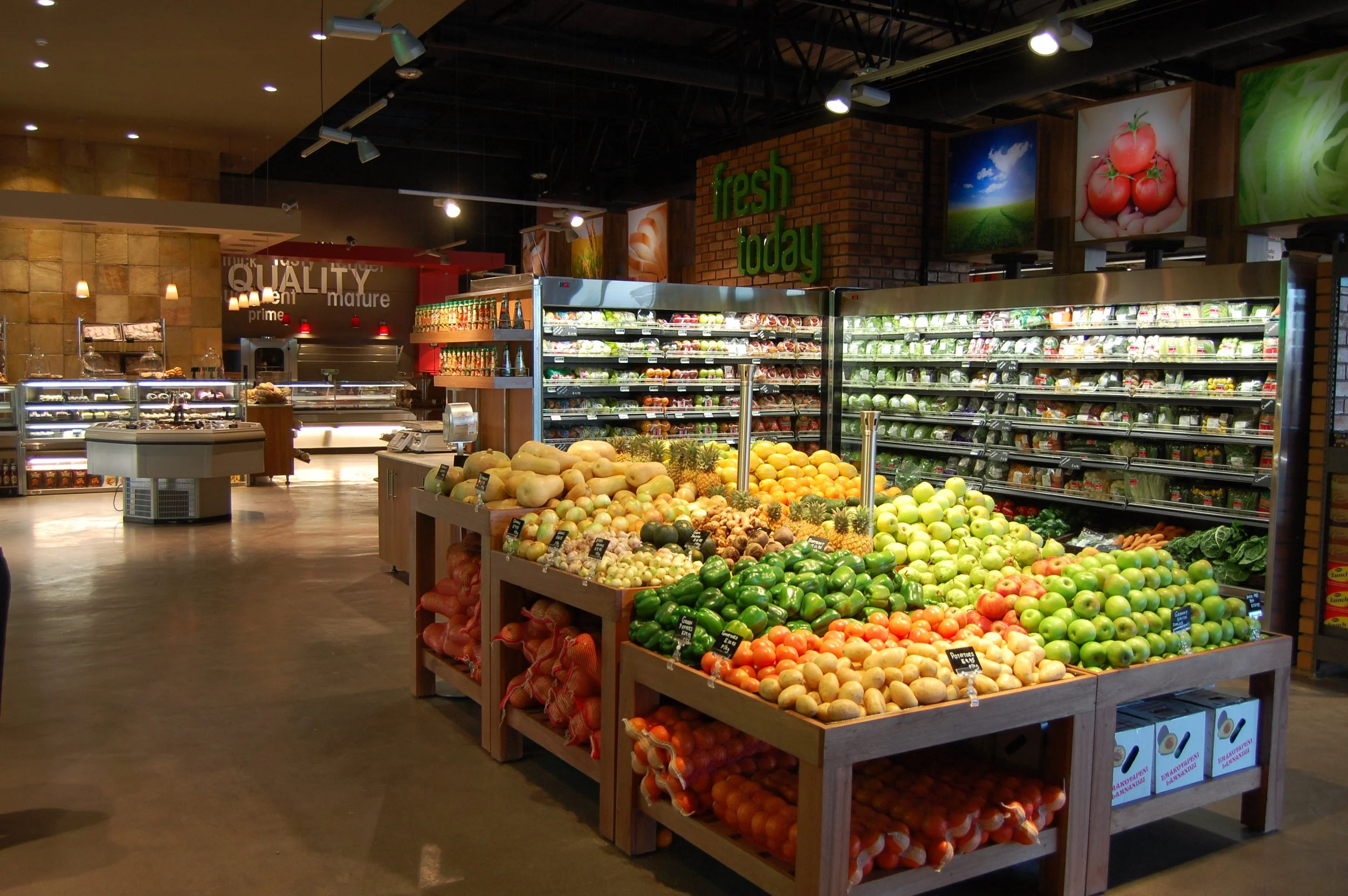 Fresh produce display in a grocery store with apples, onions, and other fruits, with shelves of packaged greens and vegetables in the background.