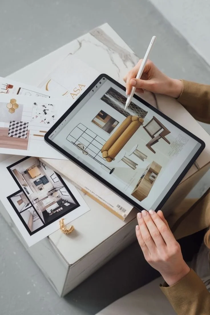 Person using a digital tablet to design an interior space, surrounded by physical fabric and material samples on a table.