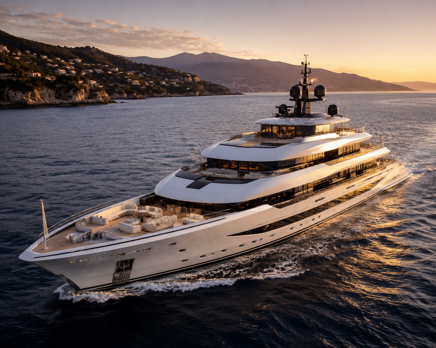 Luxury white yacht sailing at sunset near a coastline with lush hills and mountains in the background.