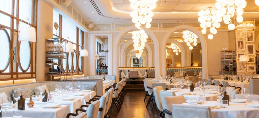 Elegant restaurant interior with white tablecloths, modern chandeliers, and plush upholstered chairs.