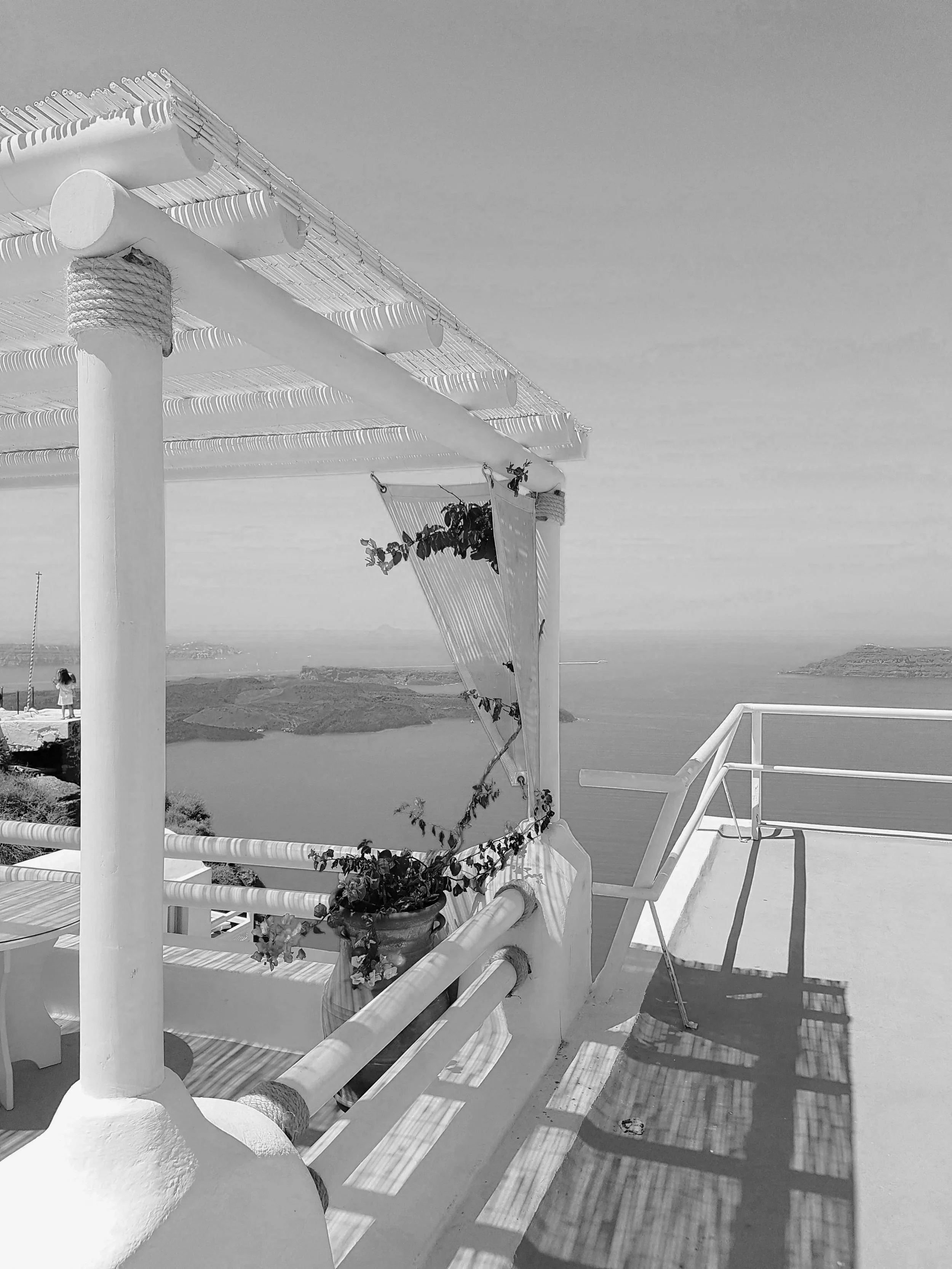 A balcony with white wooden furniture and a small potted plant, overlooking a scenic view of water and distant islands.