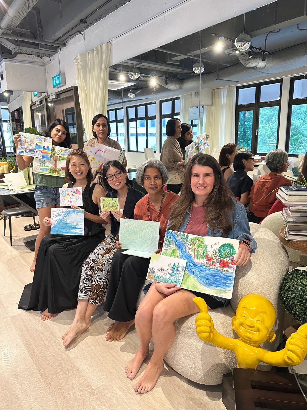 A photo of a group of women holding up their artwork in an indoor workshop setting