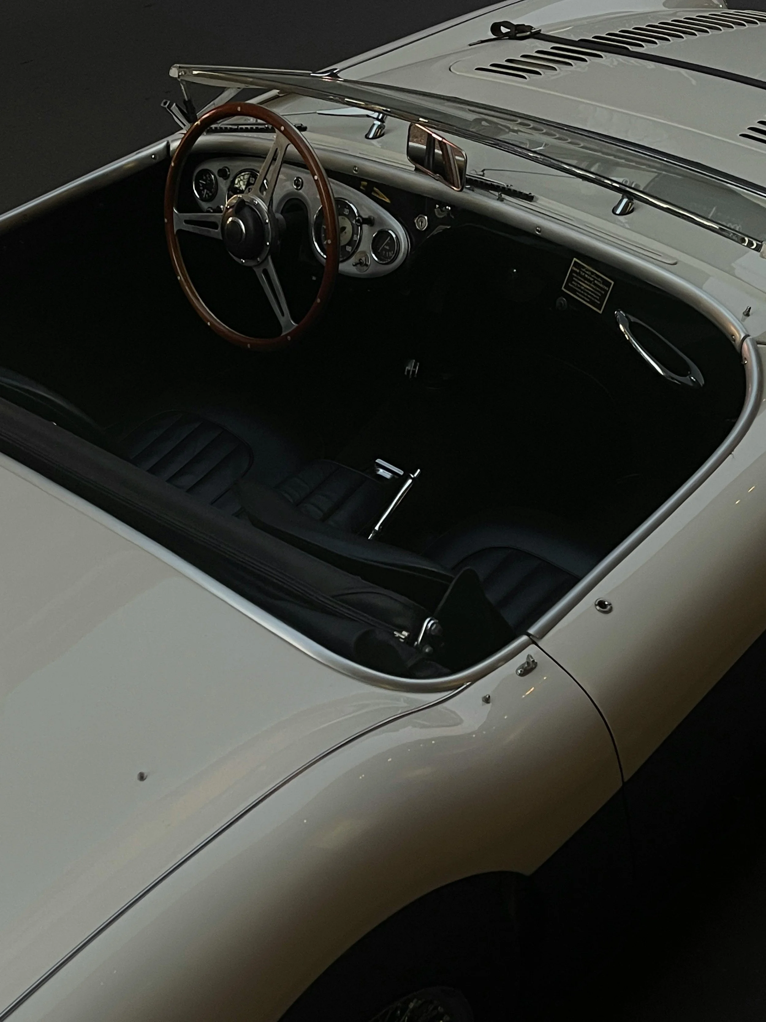 Interior view of a classic white sports car with a wooden steering wheel and black dashboard, photographed from above.