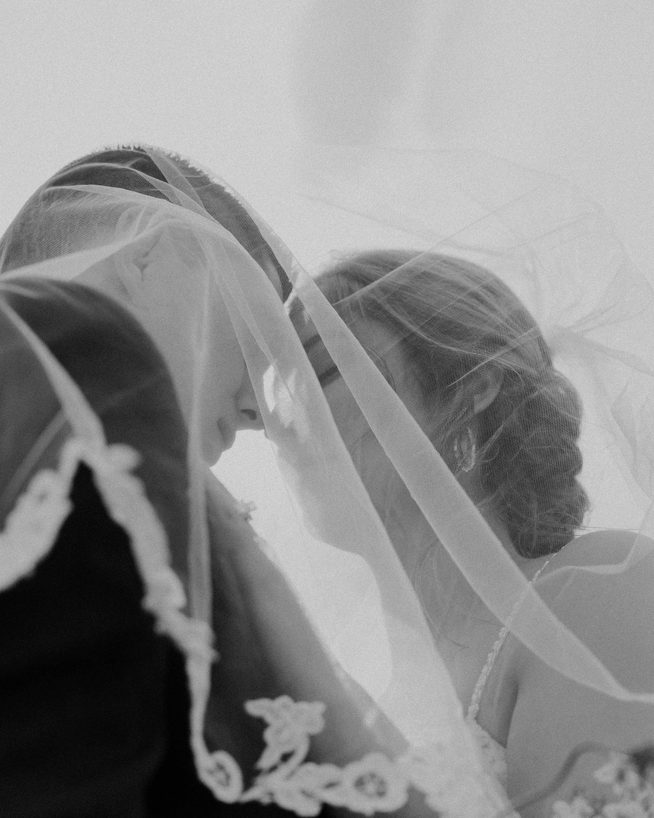 A black and white photo of a bride with a veil over her face, gazing downward, with her hair styled in an elegant updo.