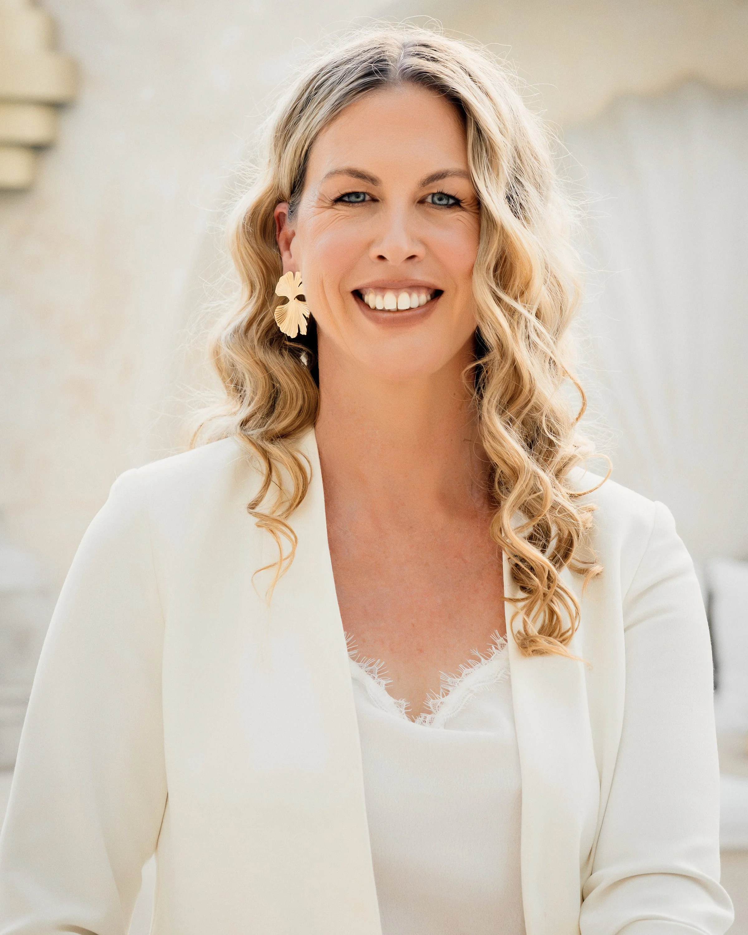 Branding woman with long brown hair, light skin, and blue eye wearing a white suit.