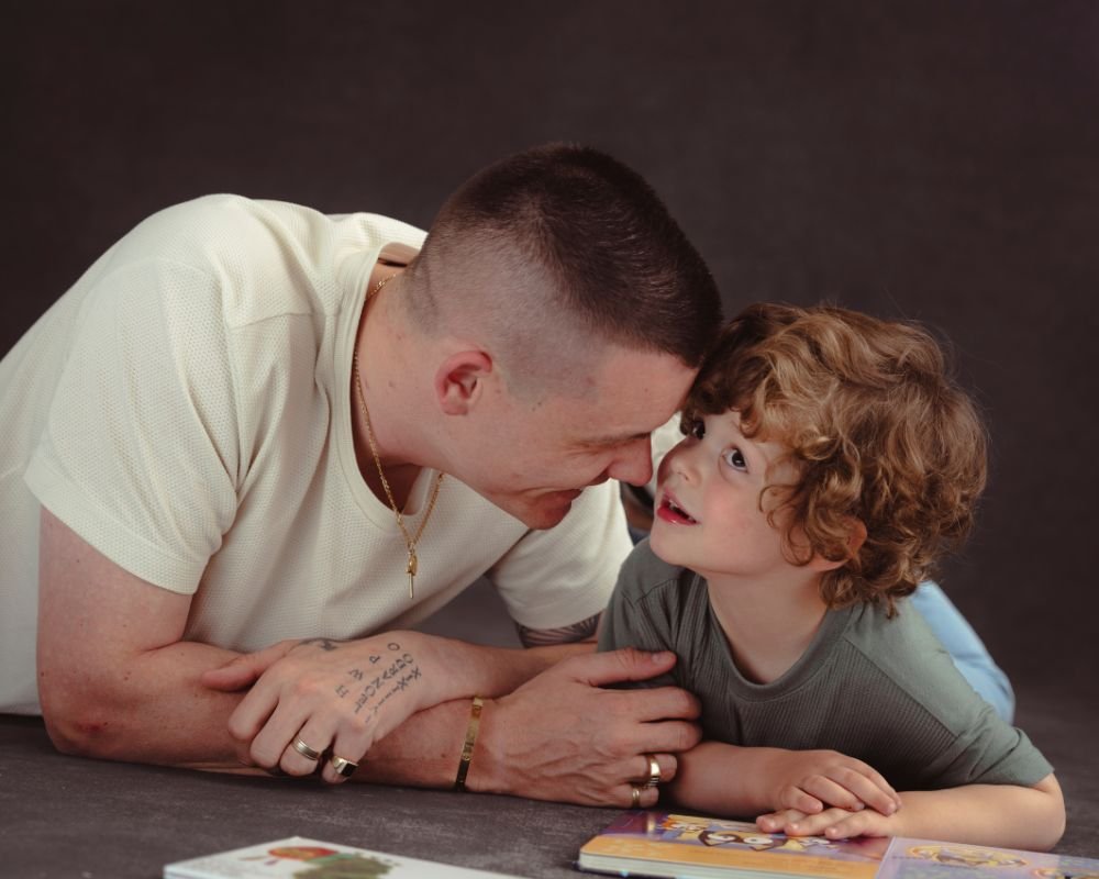 A man and young boy face to face on the floor, close together, engaged in a playful or intimate moment.