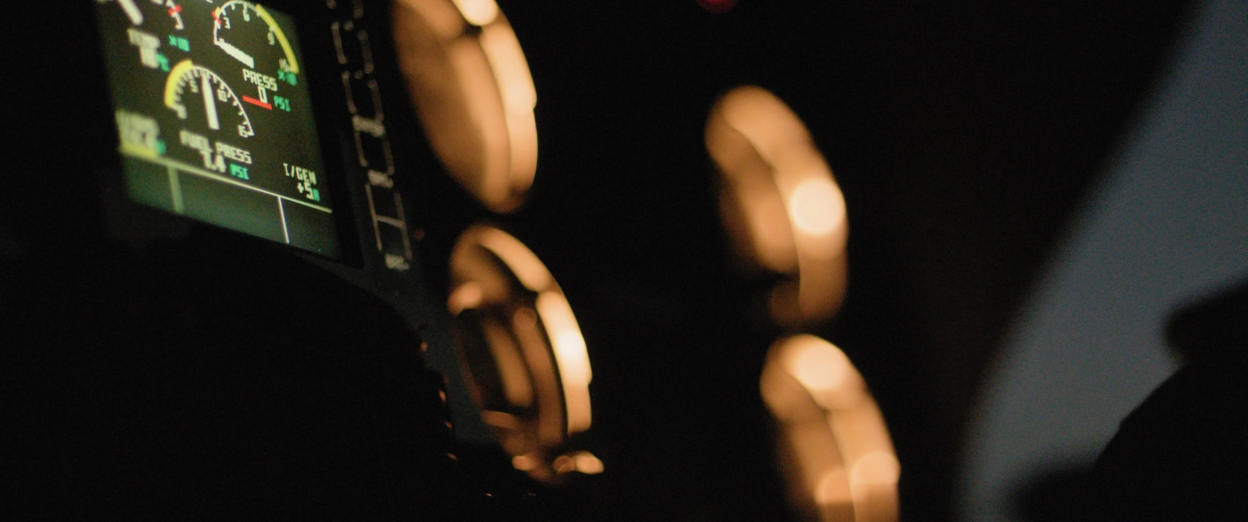 Close-up of an aircraft cockpit dashboard at night, showing illuminated gauges and controls, with a hand adjusting a dial.