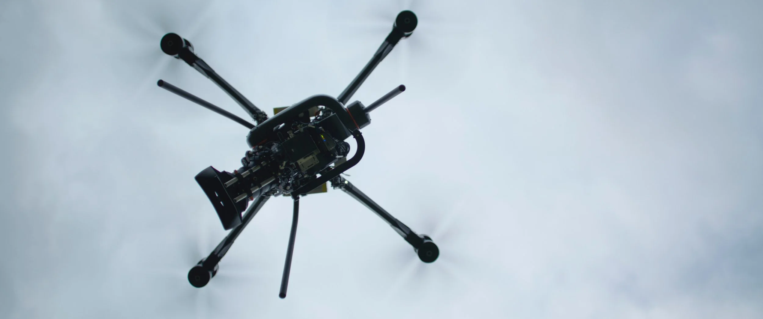 Close-up of a drone with blades spinning, flying against a cloudy sky.