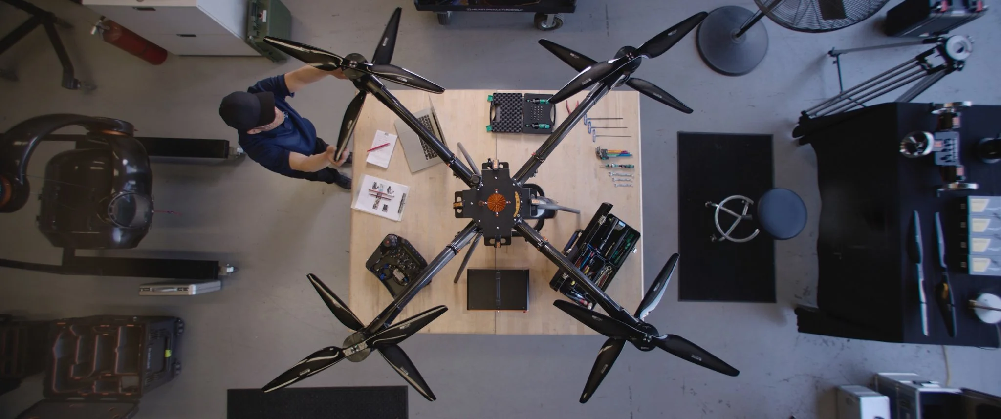 Top-down view of a person working on a multi-armed heavy lift drone with eight propellers on a workbench in a workshop.
