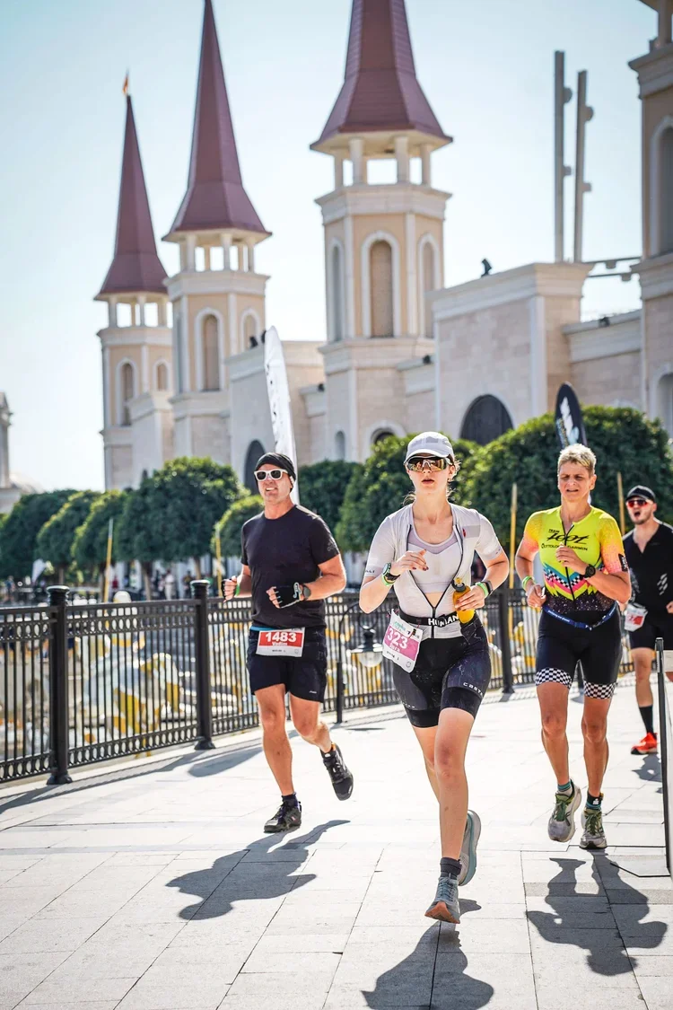 Group of runners participating in a marathon along a city street with a castle-like building in the background, sunny day.