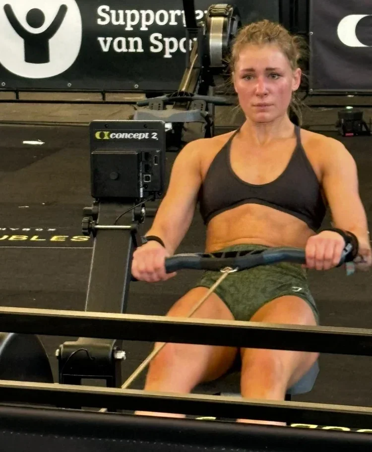 A woman with a determined expression working out on a rowing machine in a gym.