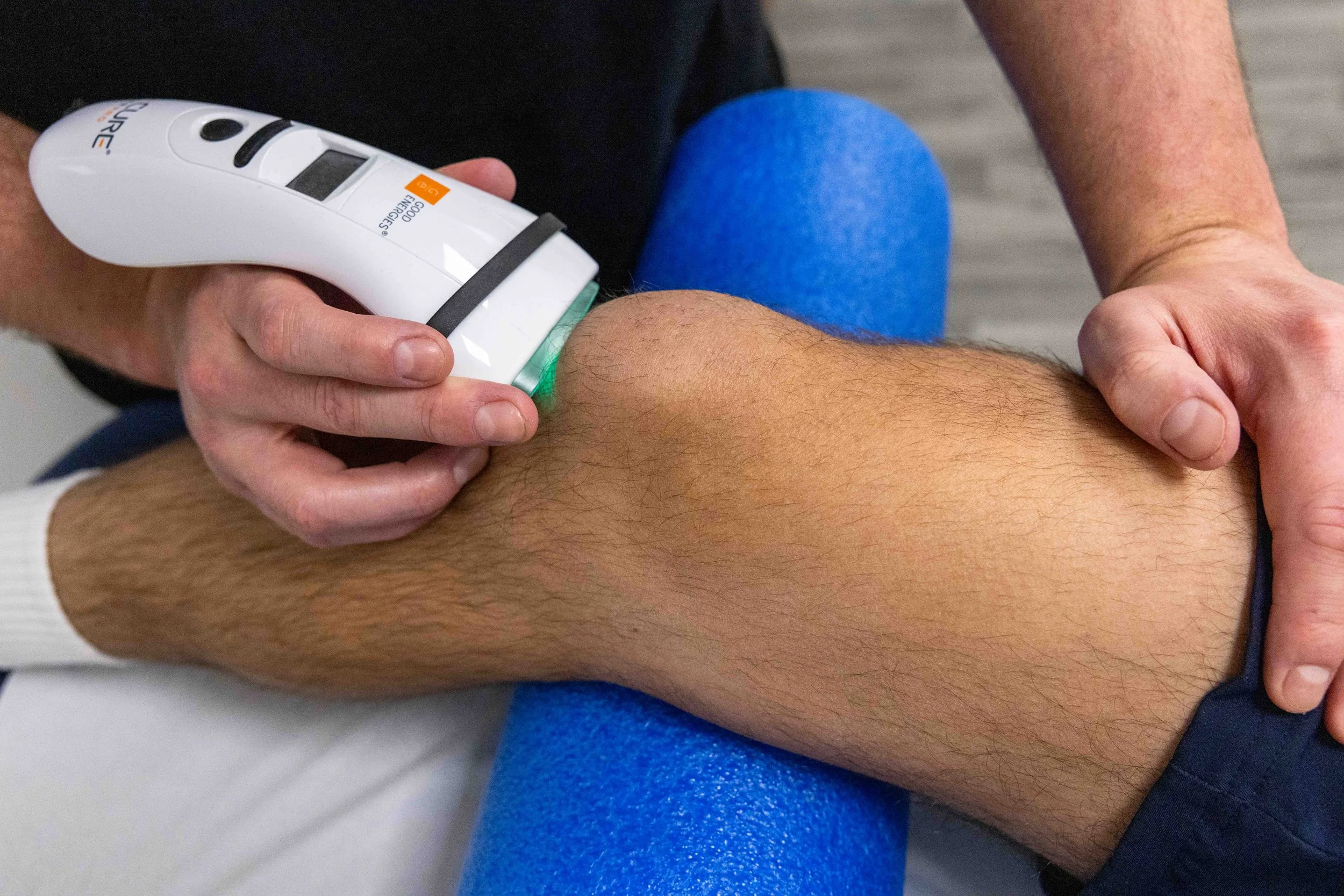 A person receiving a blood pressure measurement with a digital blood pressure monitor on their forearm, while seated on a blue cushion.