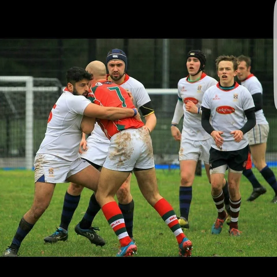 Rugby players in a game, with two players wrestling for the ball, others running nearby, on a grassy field.