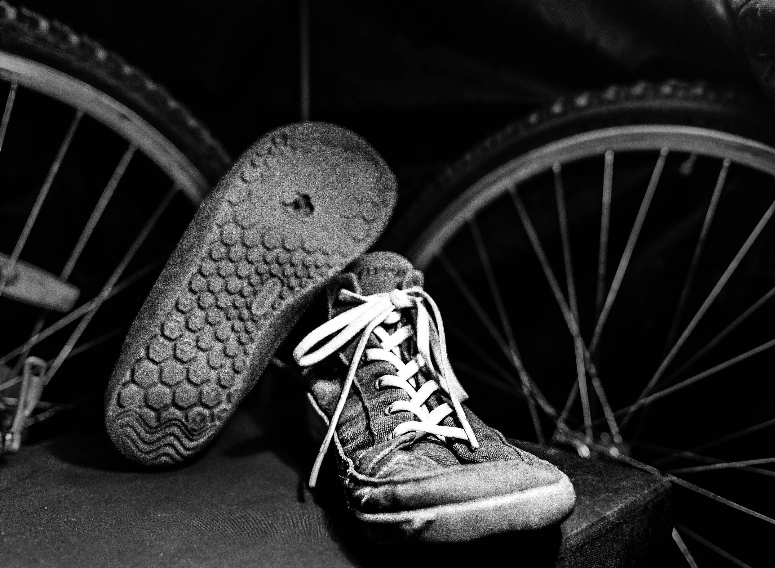 Black and white photo of a person wearing sneakers, sitting among bicycle wheels.