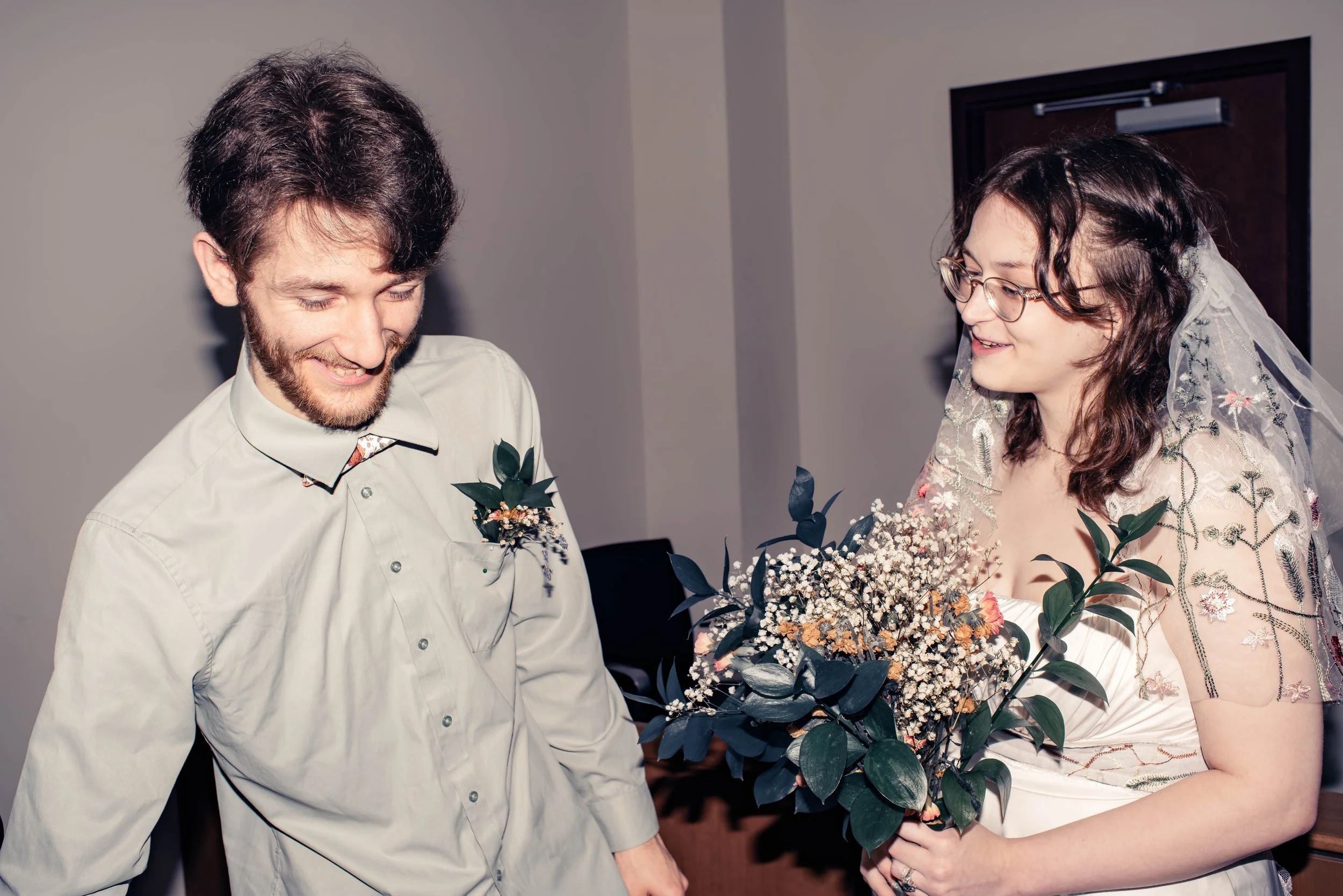 Bride smiling at her groom during an intimate wedding celebration, holding a bouquet of wildflowers and greenery.
