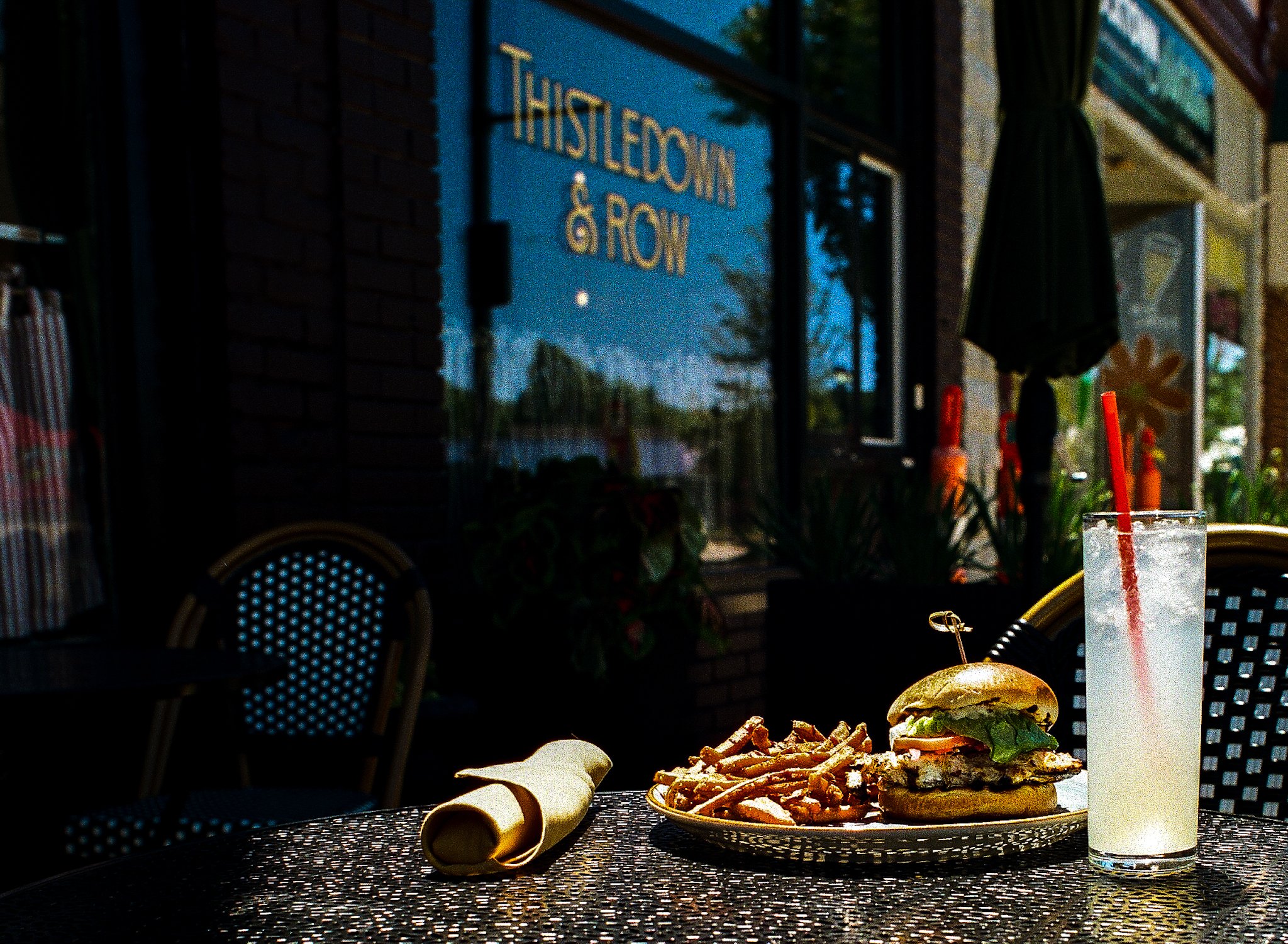 Plate of a cheeseburger with fries, a bun, and a drink with a straw on a table outside at sunset.