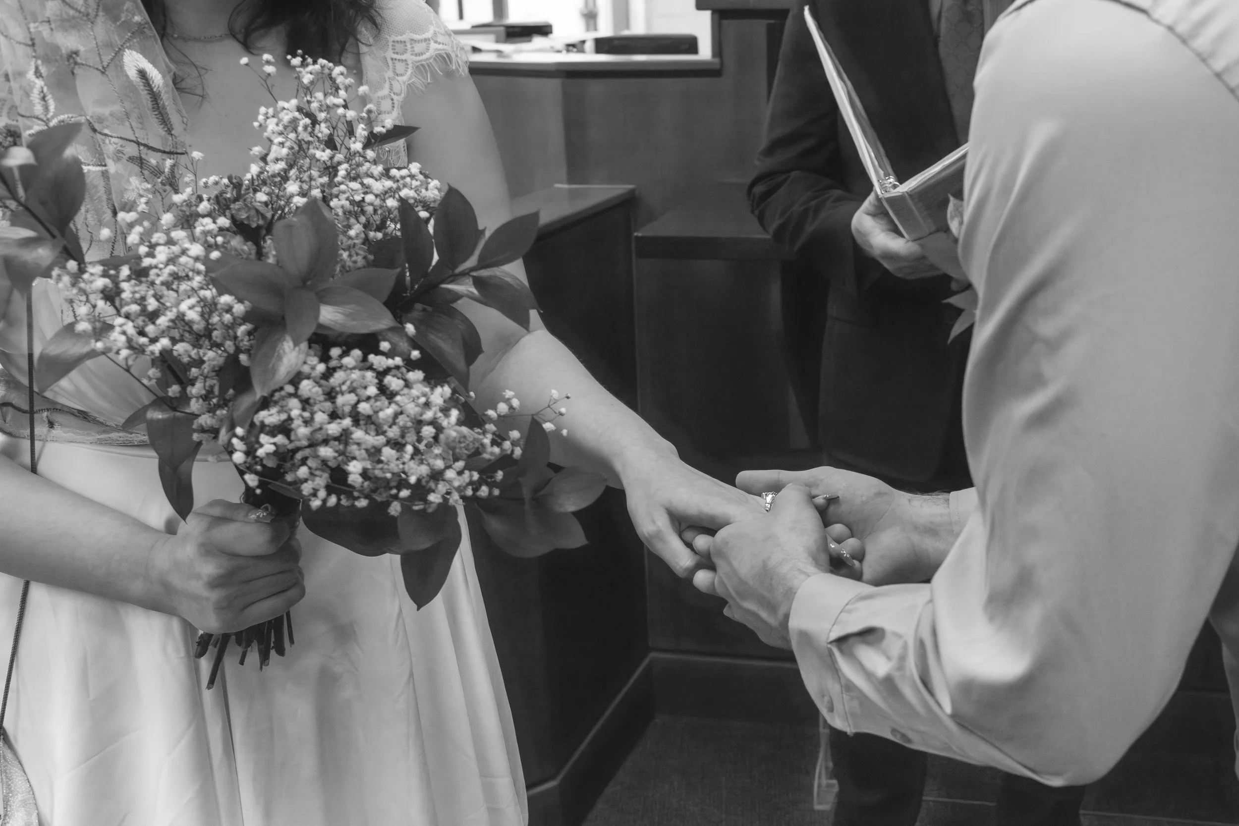 People exchanging wedding vows, with one person holding a bride's hand and wearing a wedding dress, while another person holds a bouquet of flowers.