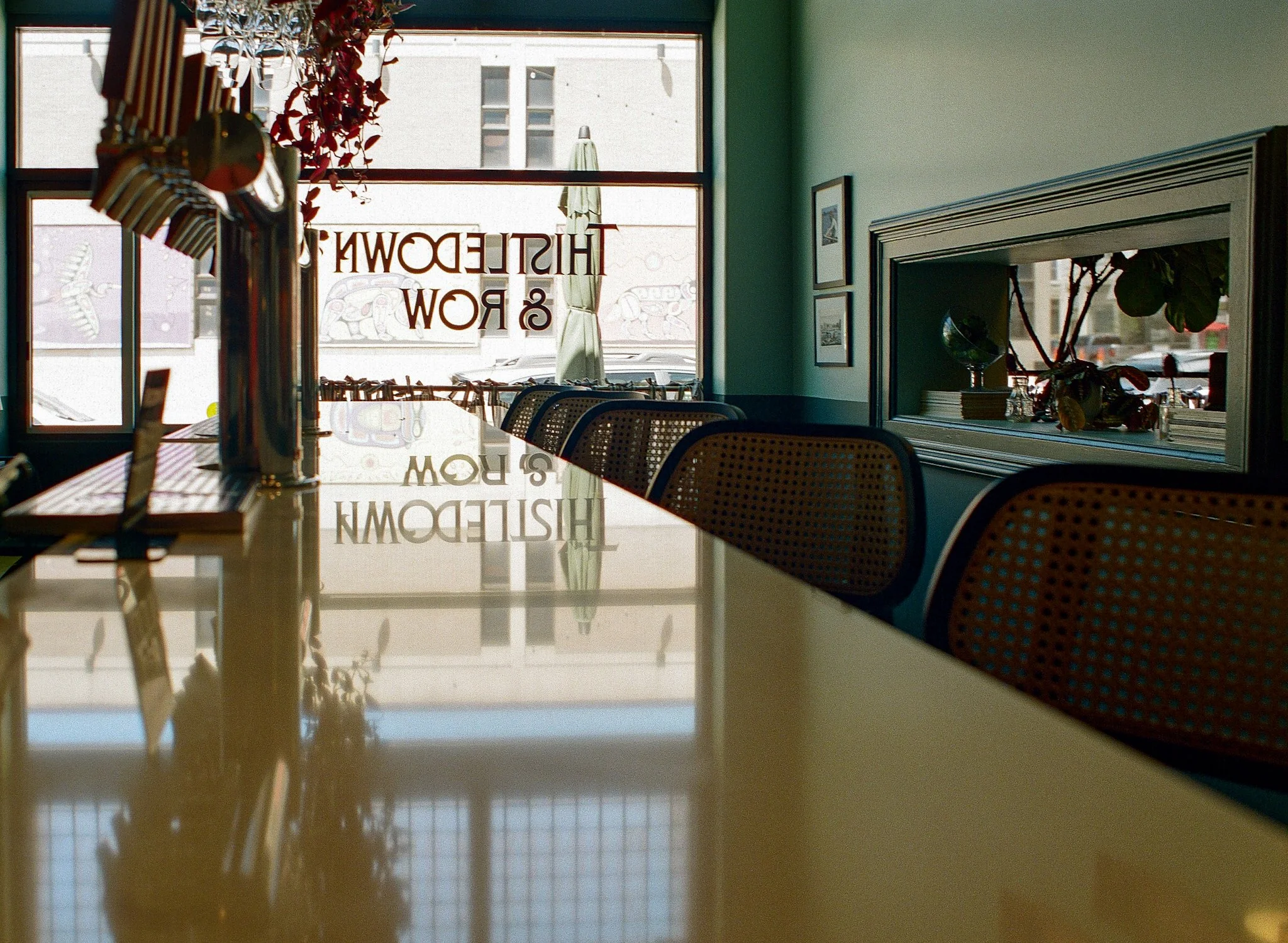 Interior of a restaurant with a table, chairs, and large windows. The words "HISTEDW & ROW" are written upside down on the glass window.