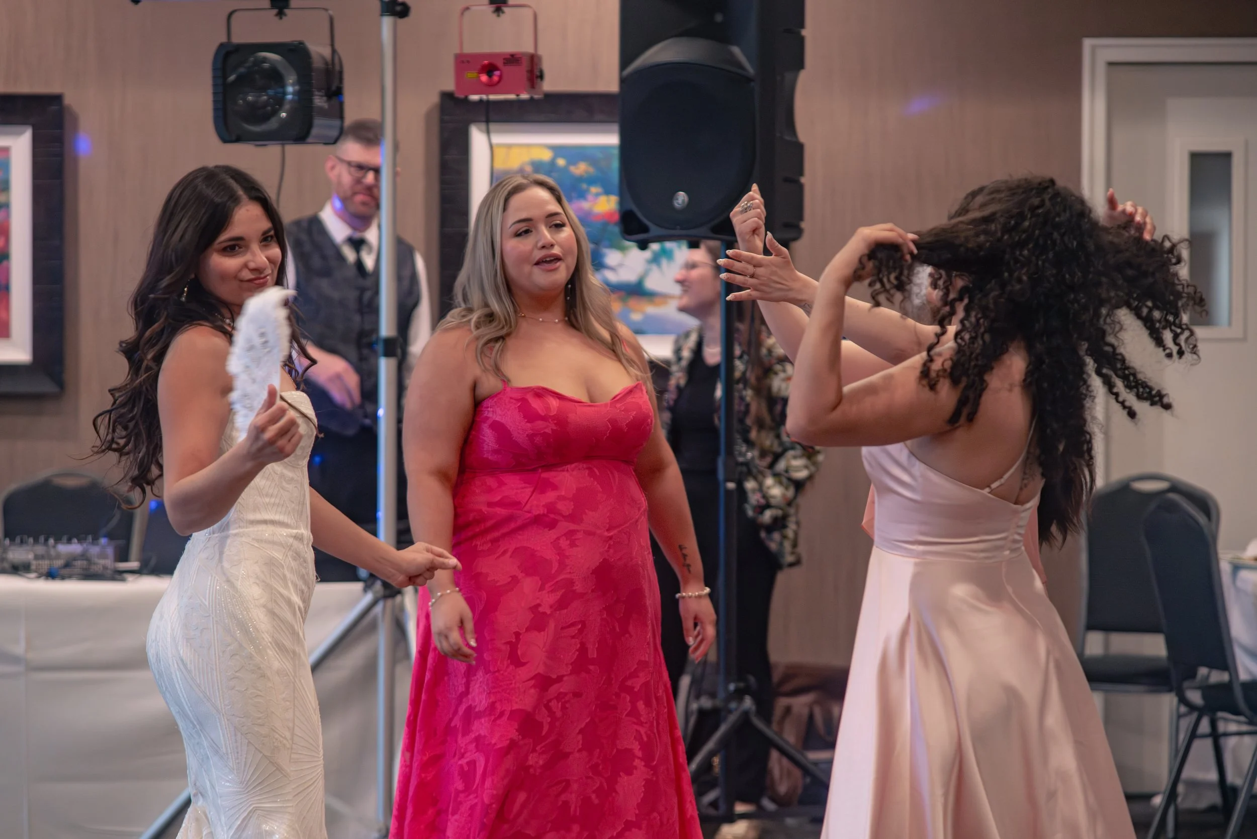 Group of women dressed in formal gowns dancing at an event with DJ equipment and speakers in the background.