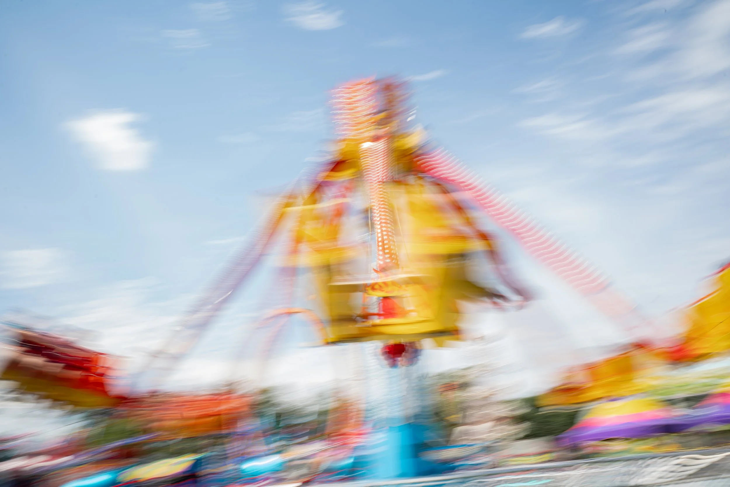 Blurred image of a colorful amusement park ride against a blue sky with some clouds.