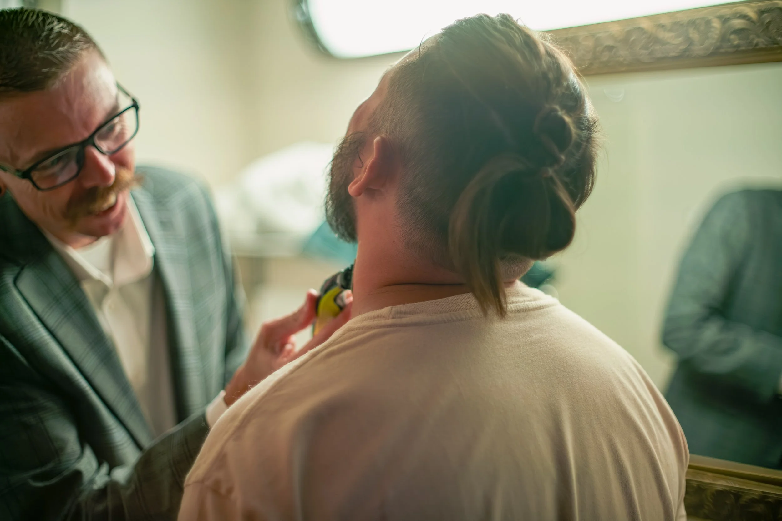 A man with glasses and a mustache giving a haircut to a person with a unique styled haircut, in a barbershop or salon.
