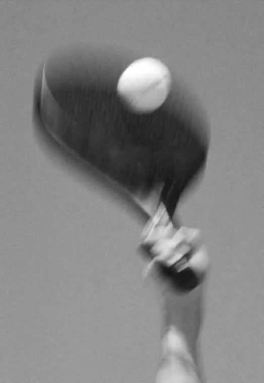 A person holding a ping pong paddle and a ping pong ball in a sports setting.