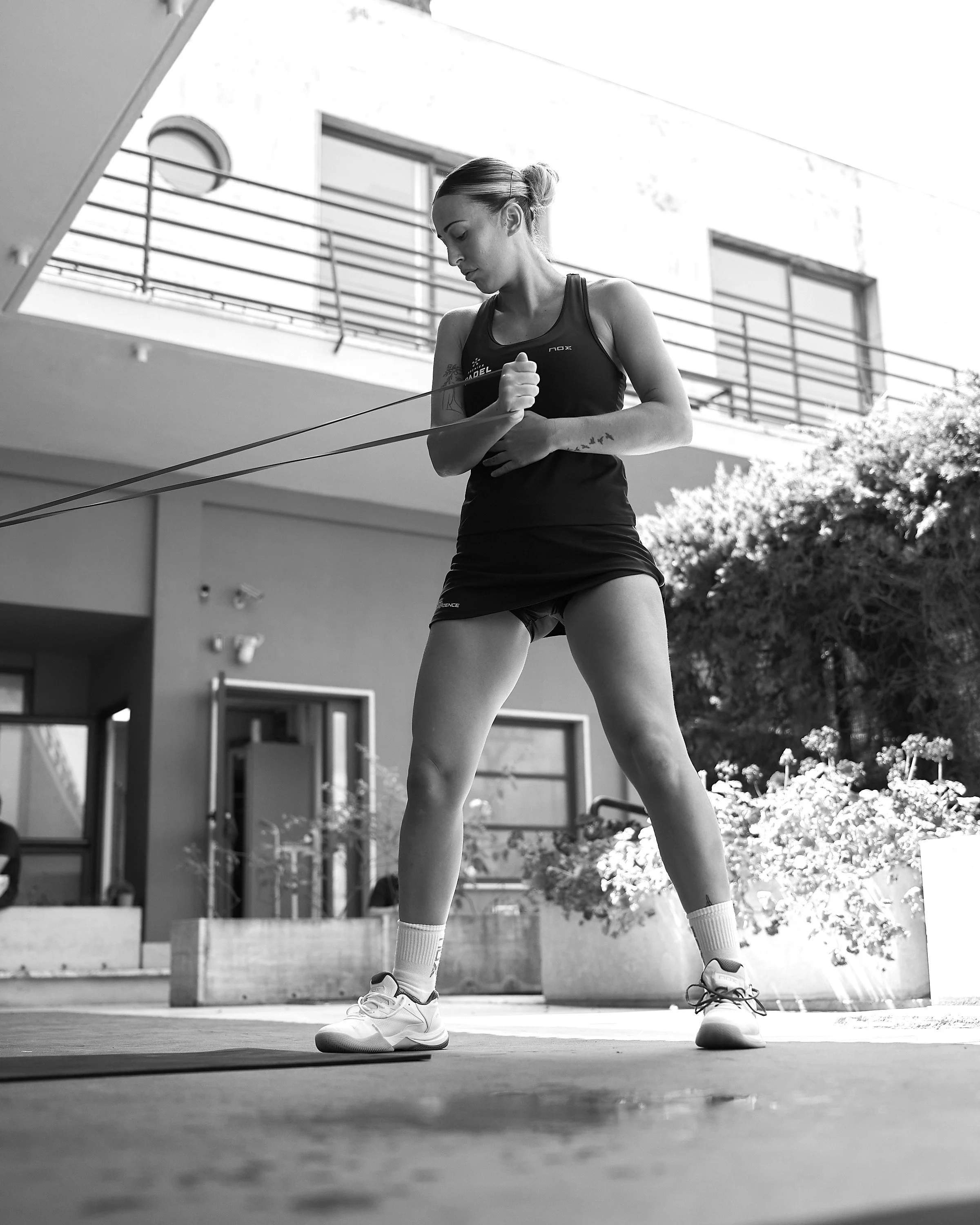 A woman in athletic clothing is preparing to play basketball on an outdoor court, standing with her legs apart.